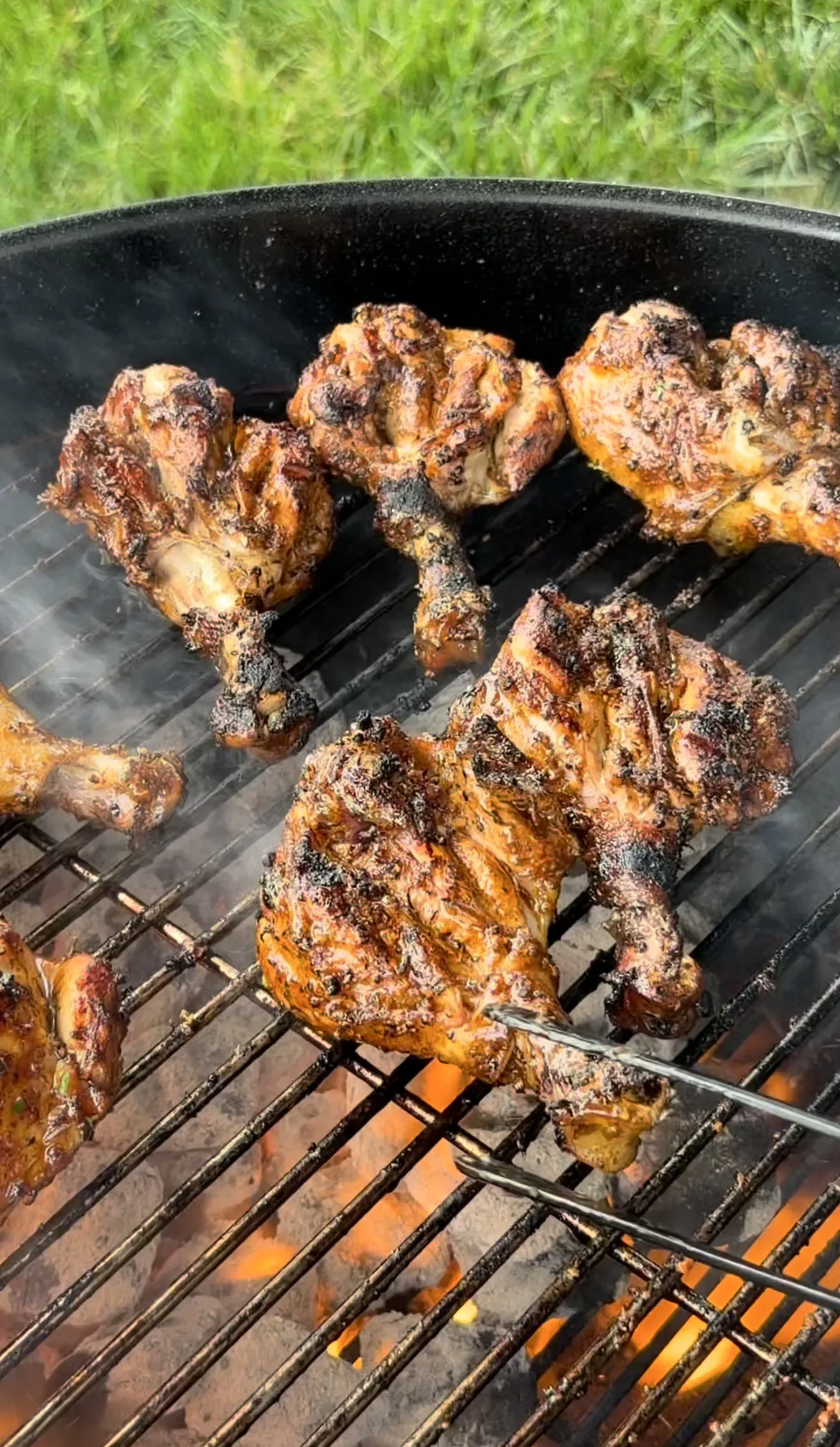 Spicy Cajun-seasoned chicken drumsticks grilling over open flames on a charcoal grill with tongs