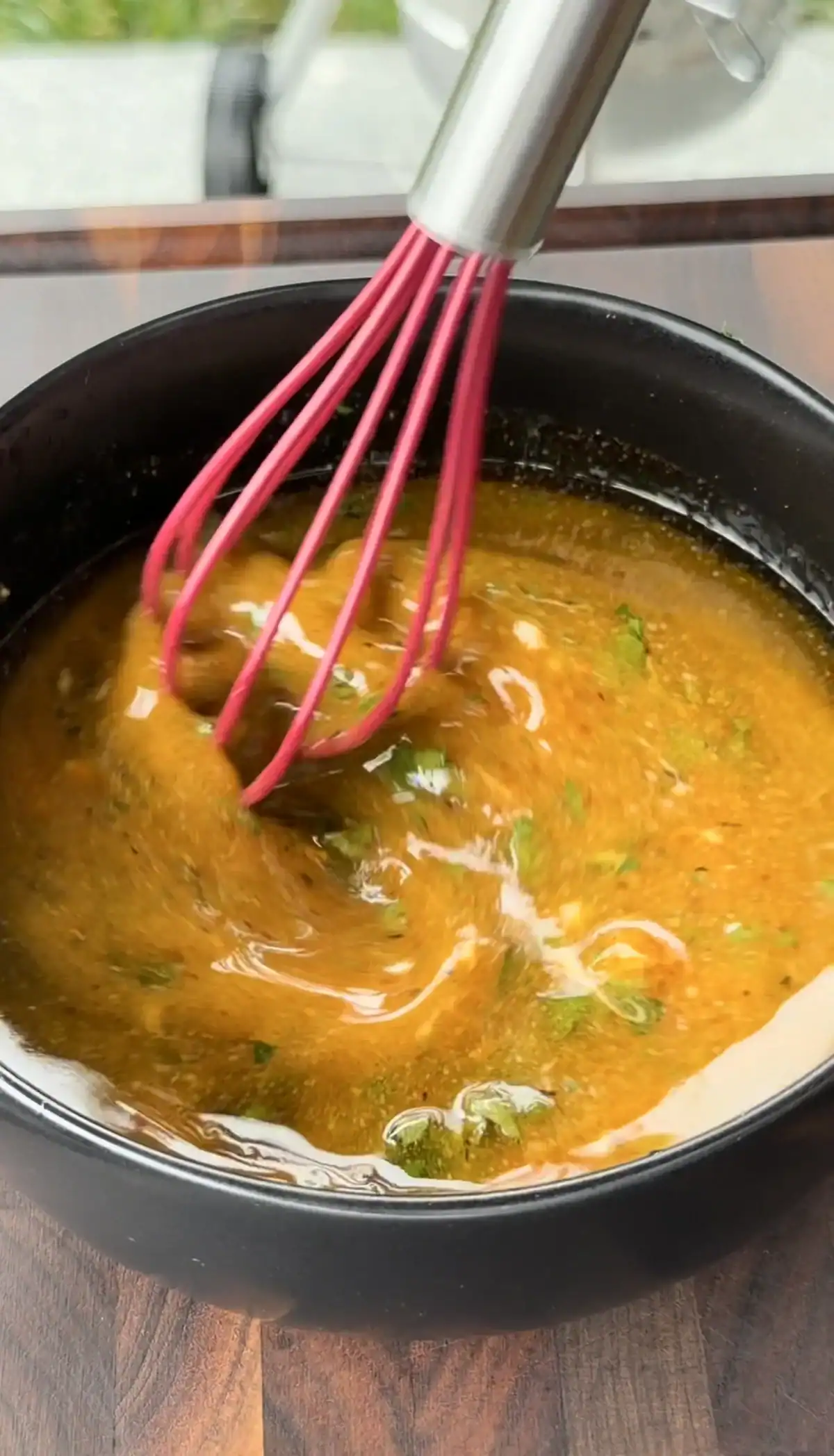 Spicy Cajun chicken marinade with herbs being whisked in a black bowl with a pink silicone whisk.