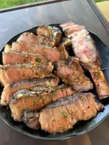 Grilled beef ribs sliced and piled on a black plate, coated in chili parmesan compound butter with herbs and garlic