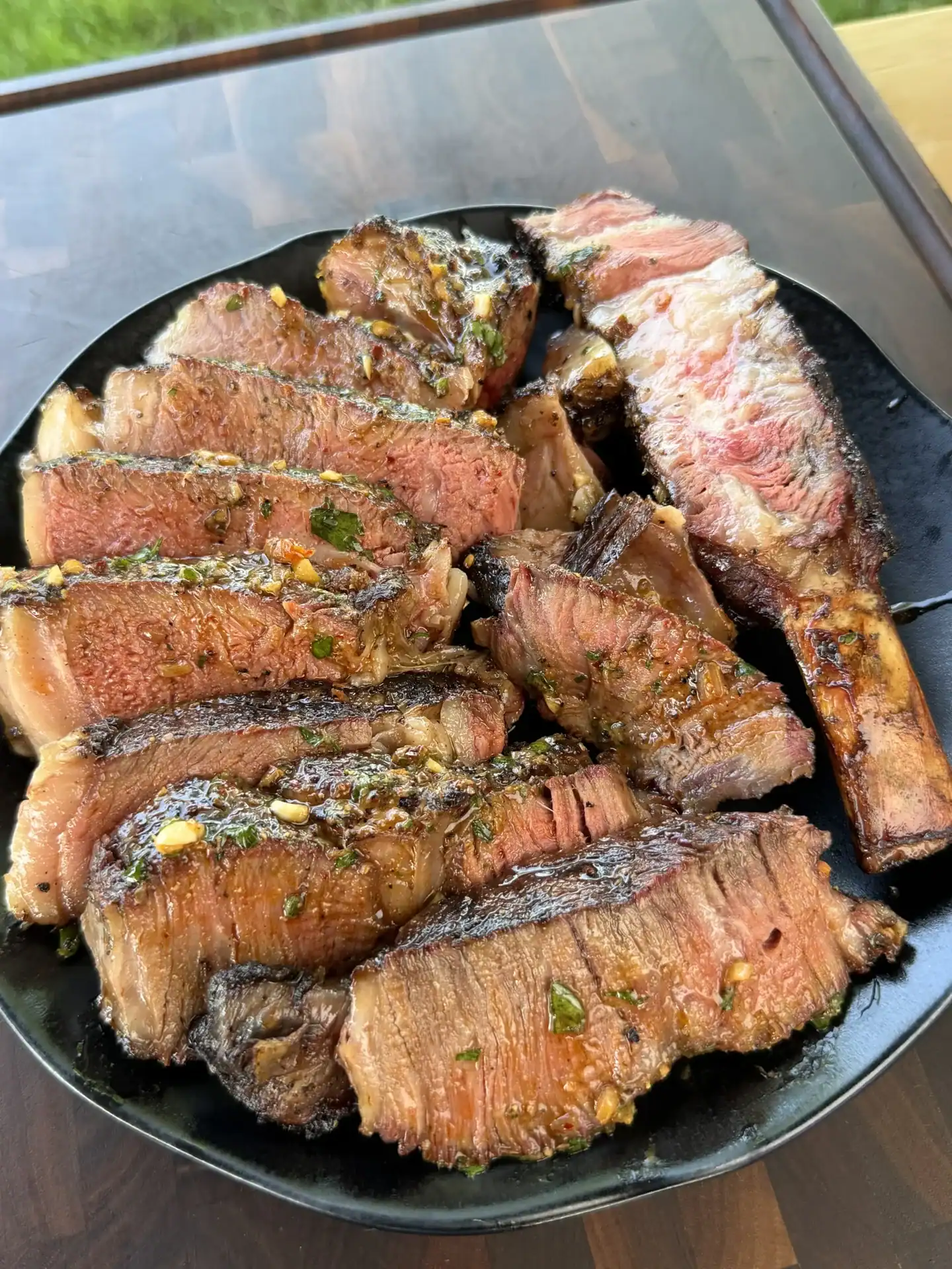 Grilled beef ribs sliced and piled on a black plate, coated in chili parmesan compound butter with herbs and garlic
