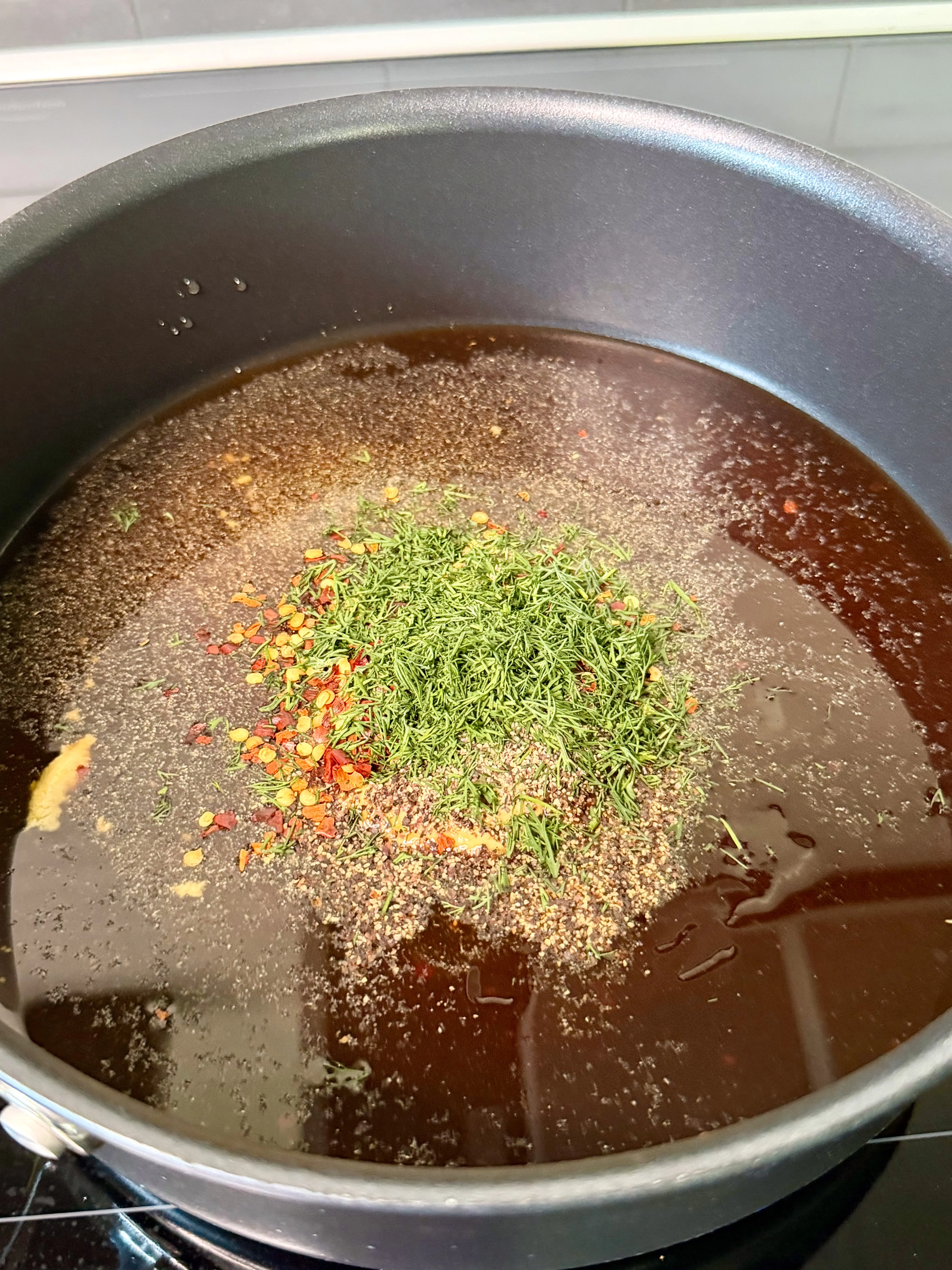 Dark dill pickle hot honey glaze with dill, red pepper flakes, and spices simmering in a large pan