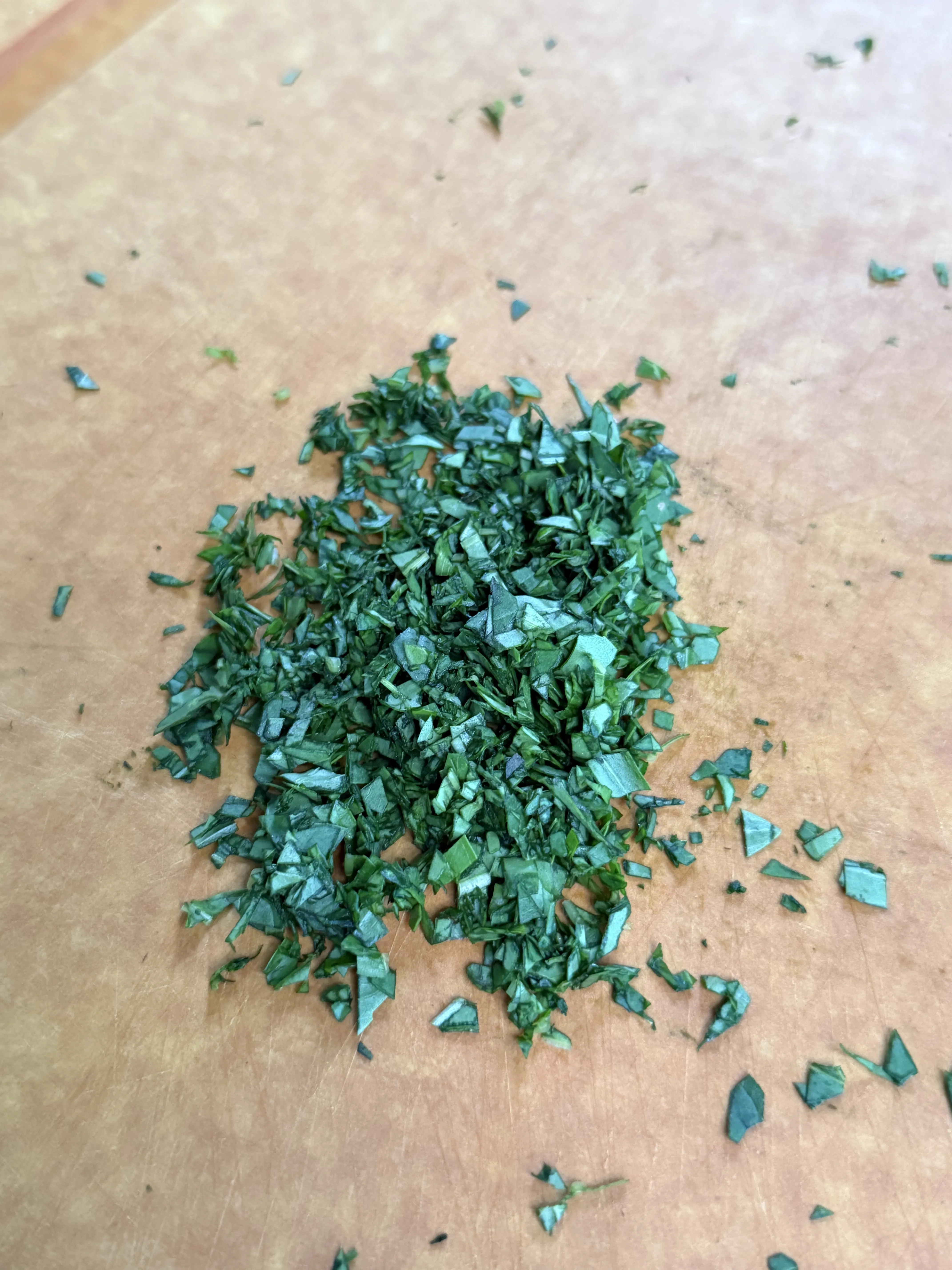 Finely chopped fresh basil piled on a wooden cutting board
