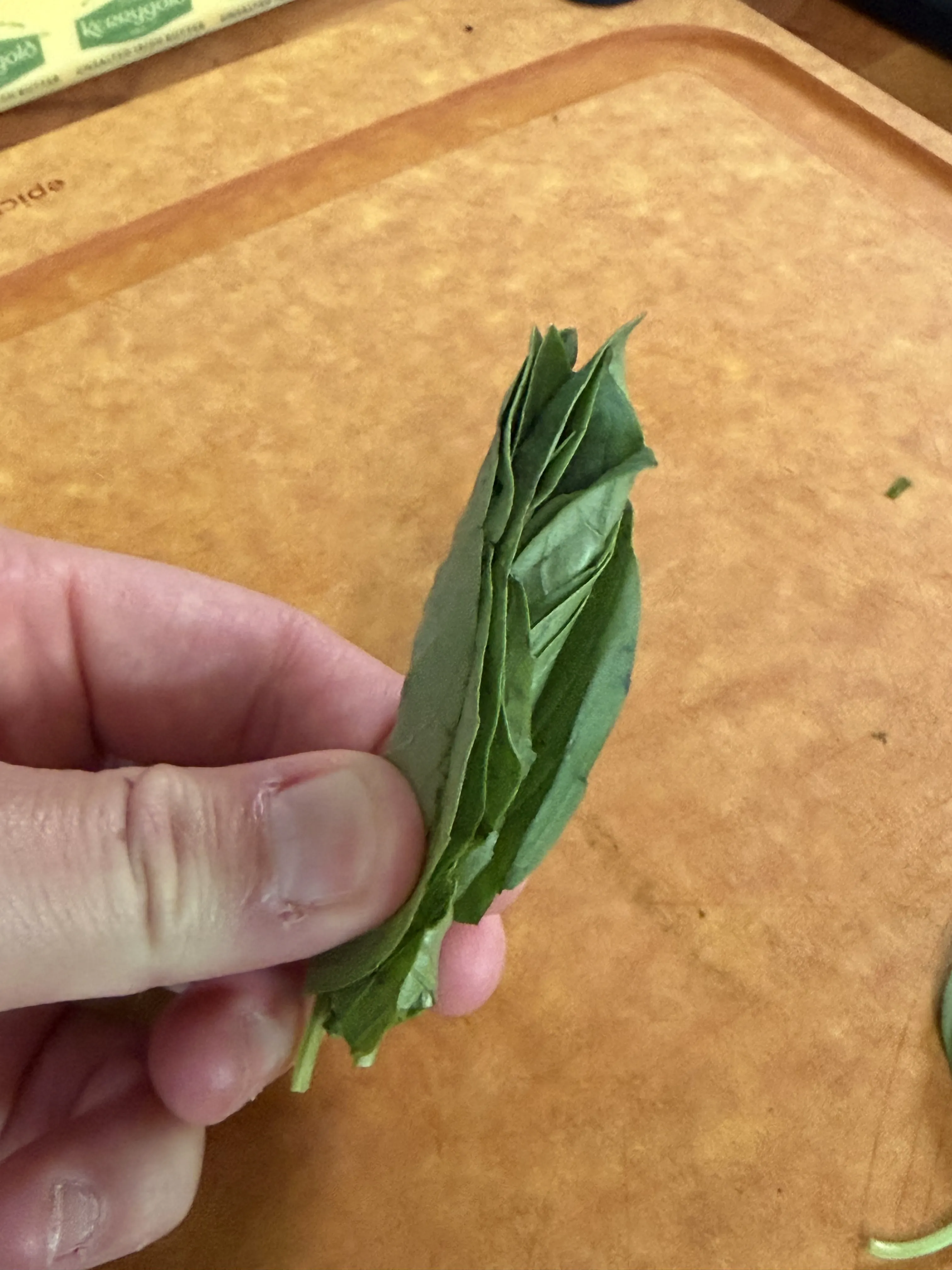 Hand rolling a stack of fresh basil leaves for chiffonade over a cutting board