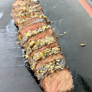 Sliced grilled steak topped with garlic parmesan basil compound butter on a black slate board