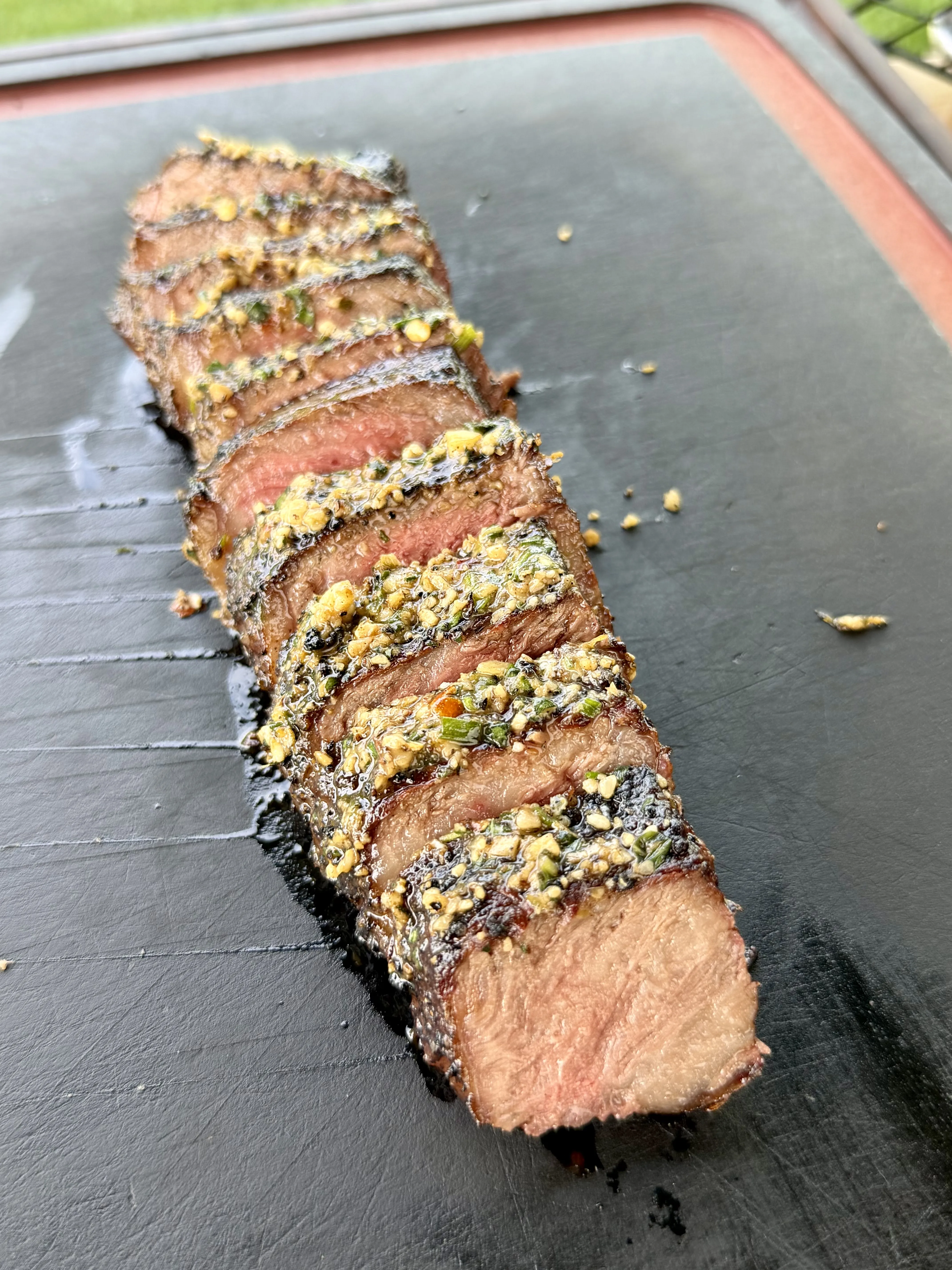 Grilled steak sliced and finished with melting basil compound butter on a slate board