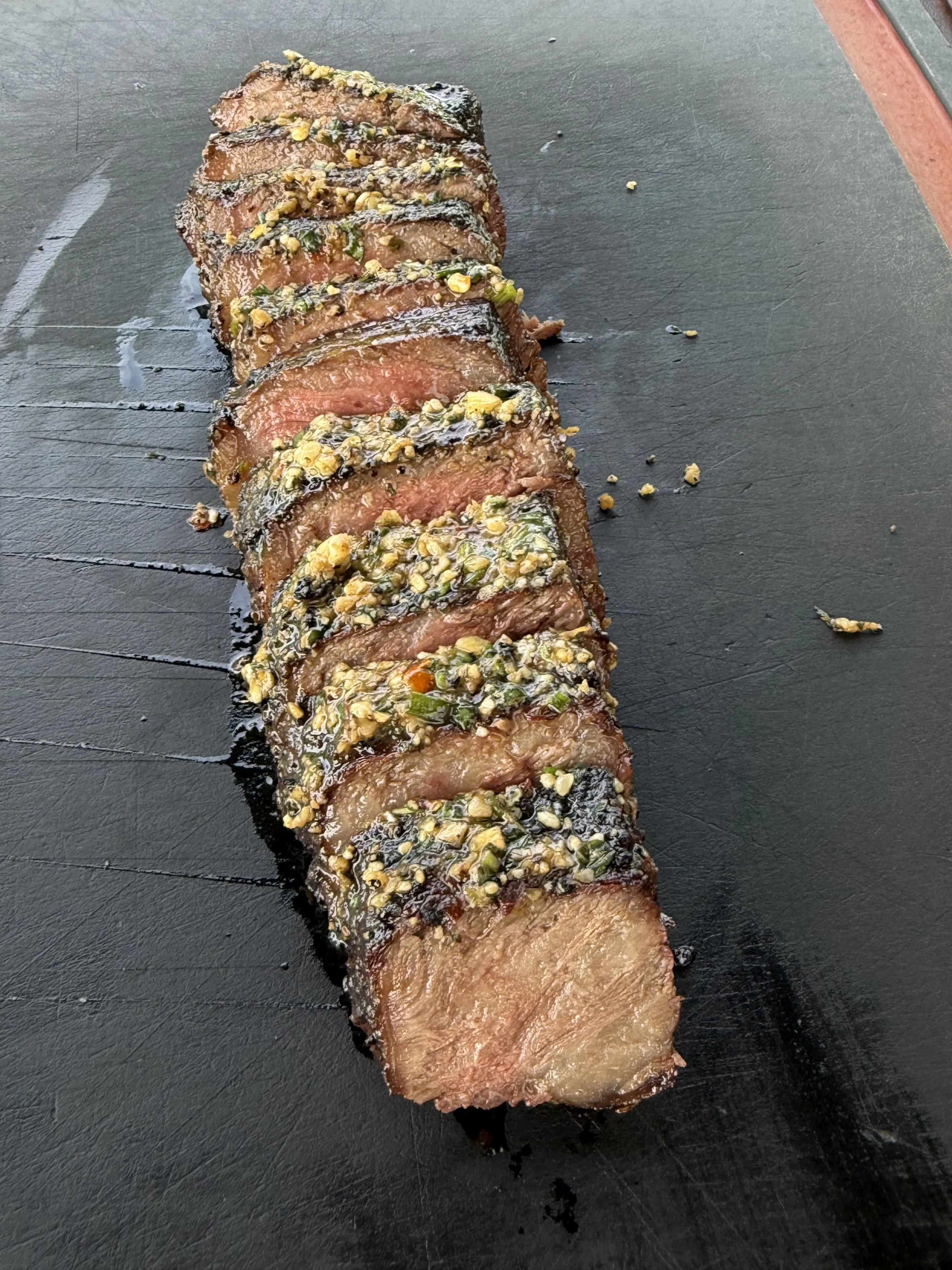 Rounds of compound butter melting over sliced grilled steak on slate