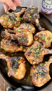 Juicy grilled Cajun chicken drumsticks in a cast iron skillet, garnished with fresh herbs and Weber N'Orleans Cajun seasoning nearby