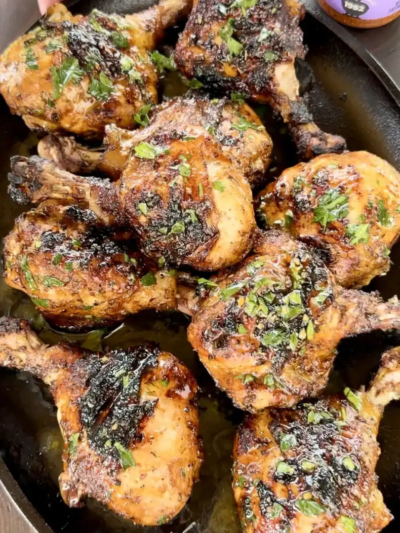 Juicy grilled Cajun chicken drumsticks in a cast iron skillet, garnished with fresh herbs and Weber N'Orleans Cajun seasoning nearby