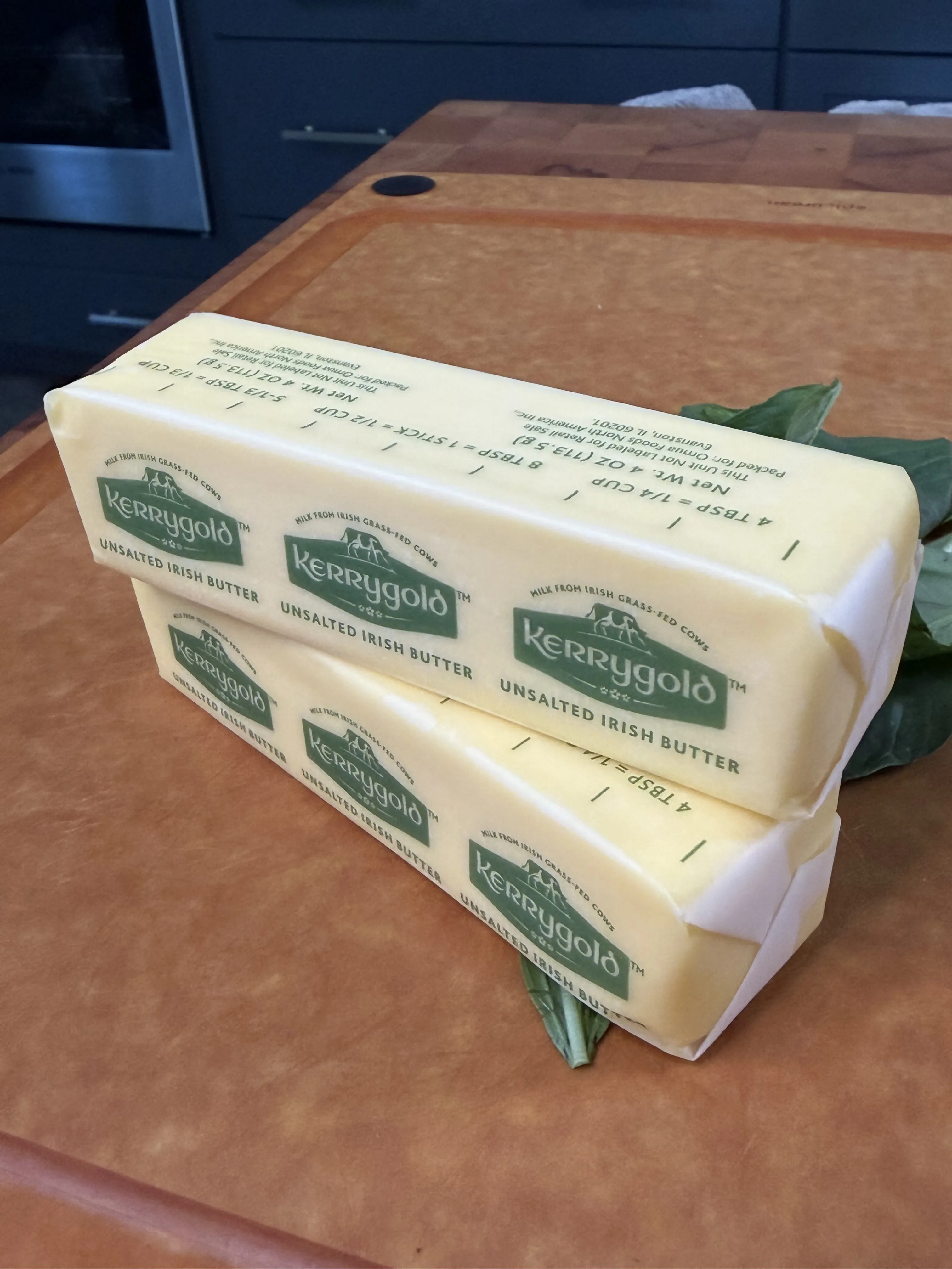 Two blocks of unsalted butter stacked on a cutting board with fresh basil