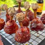 Glazed bacon-wrapped chicken lollipops with foil-tipped bones on a wire rack, coated in molasses BBQ glaze
