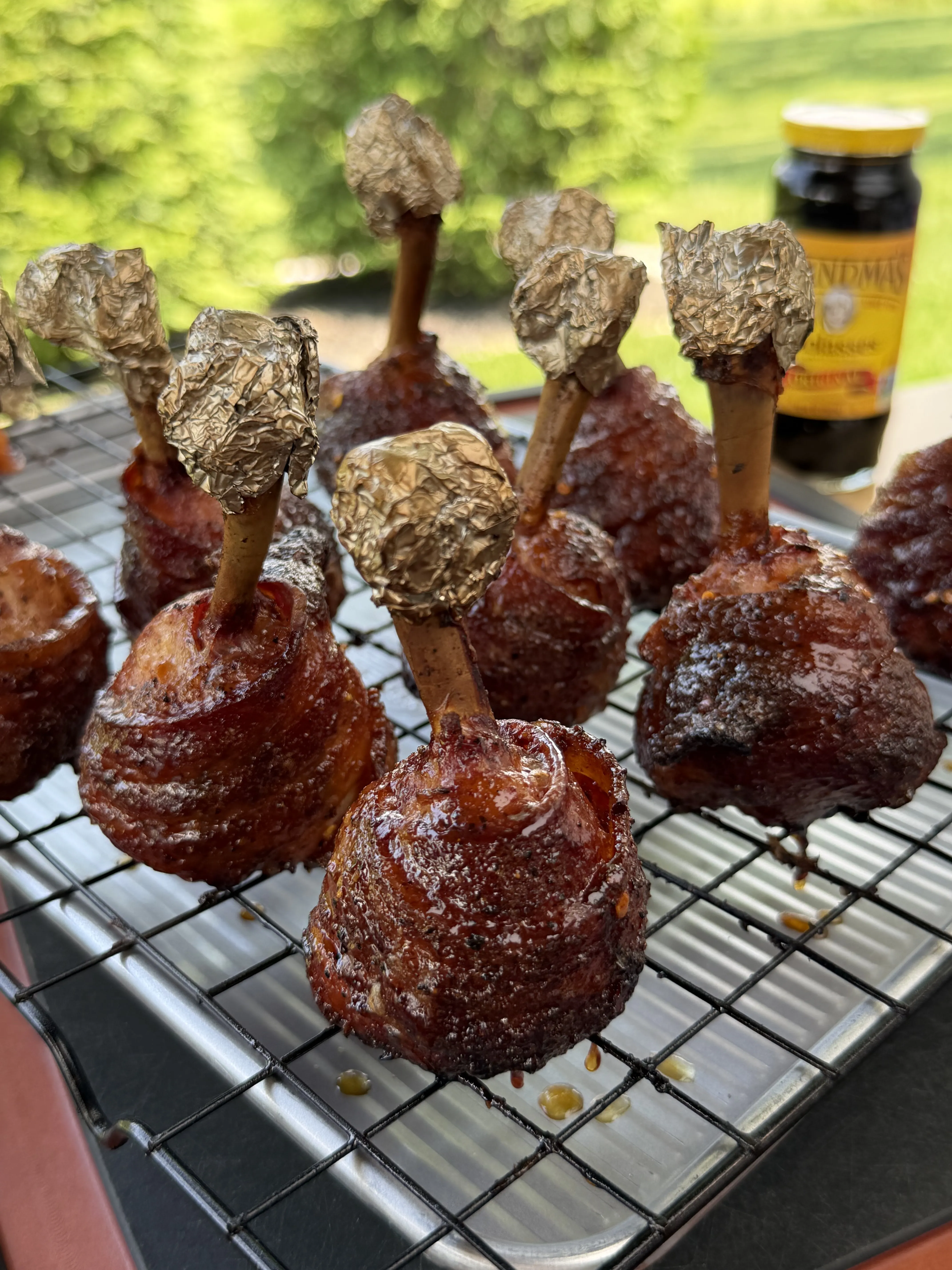 Molasses candied bacon wrapped chicken lollipops glazed and resting on a wire rack