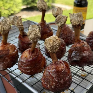 Bacon-wrapped chicken lollipops glazed with molasses on a grill rack, bones wrapped in foil, outdoors
