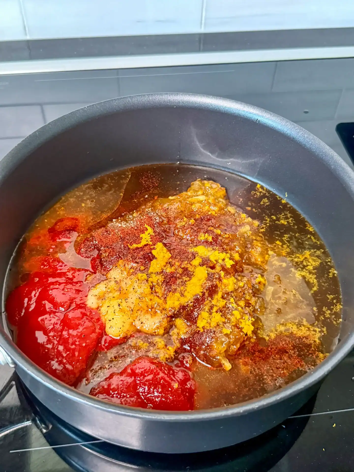 Orange gochujang BBQ sauce with tomatoes, turmeric, and spices simmering in a large pot on stovetop.