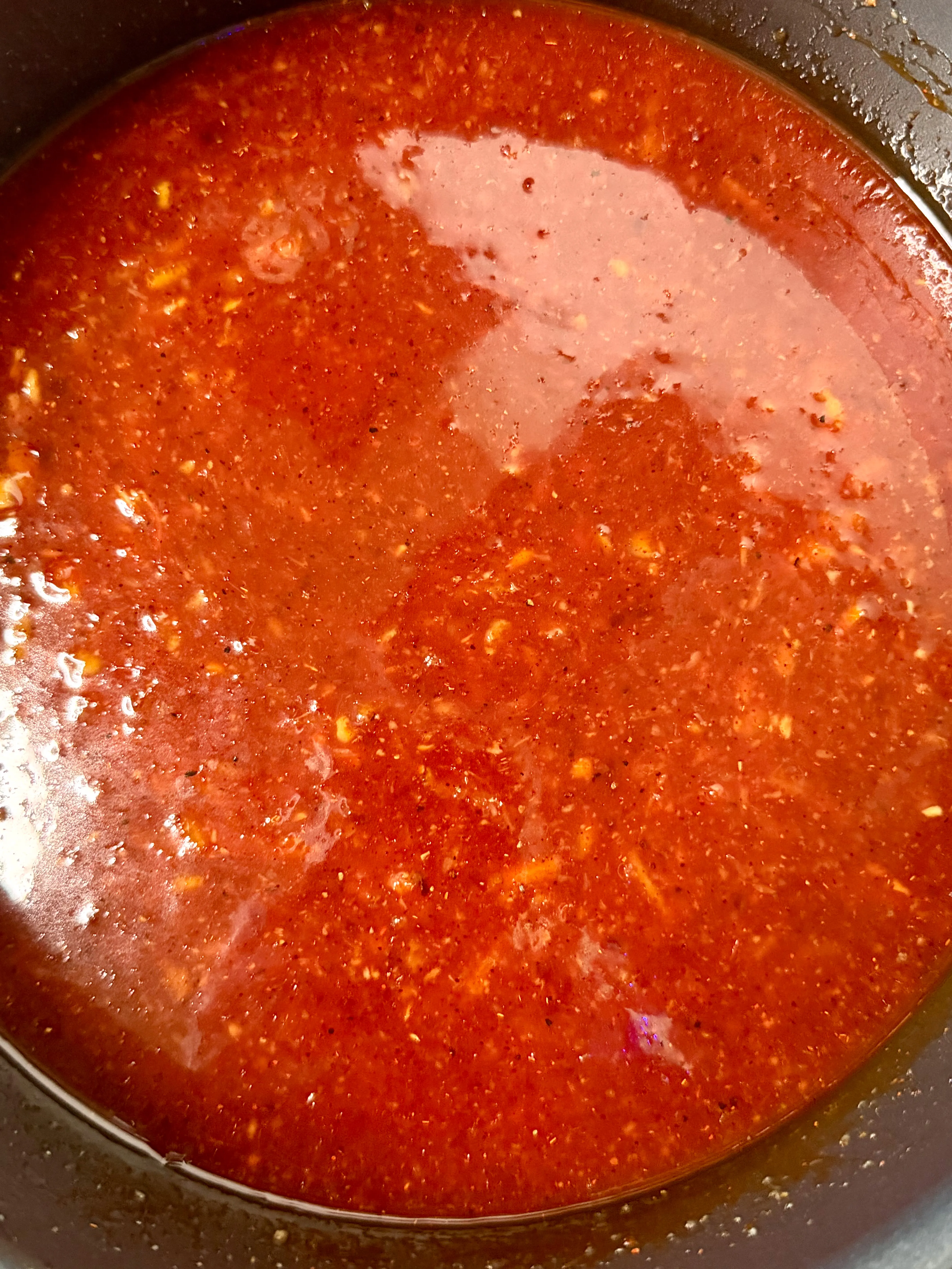 Red-orange gochujang BBQ sauce simmering with visible citrus zest until thick and glossy