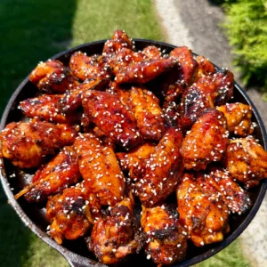 Glazed orange gochujang BBQ smoked chicken wings topped with sesame seeds served in a cast iron skillet