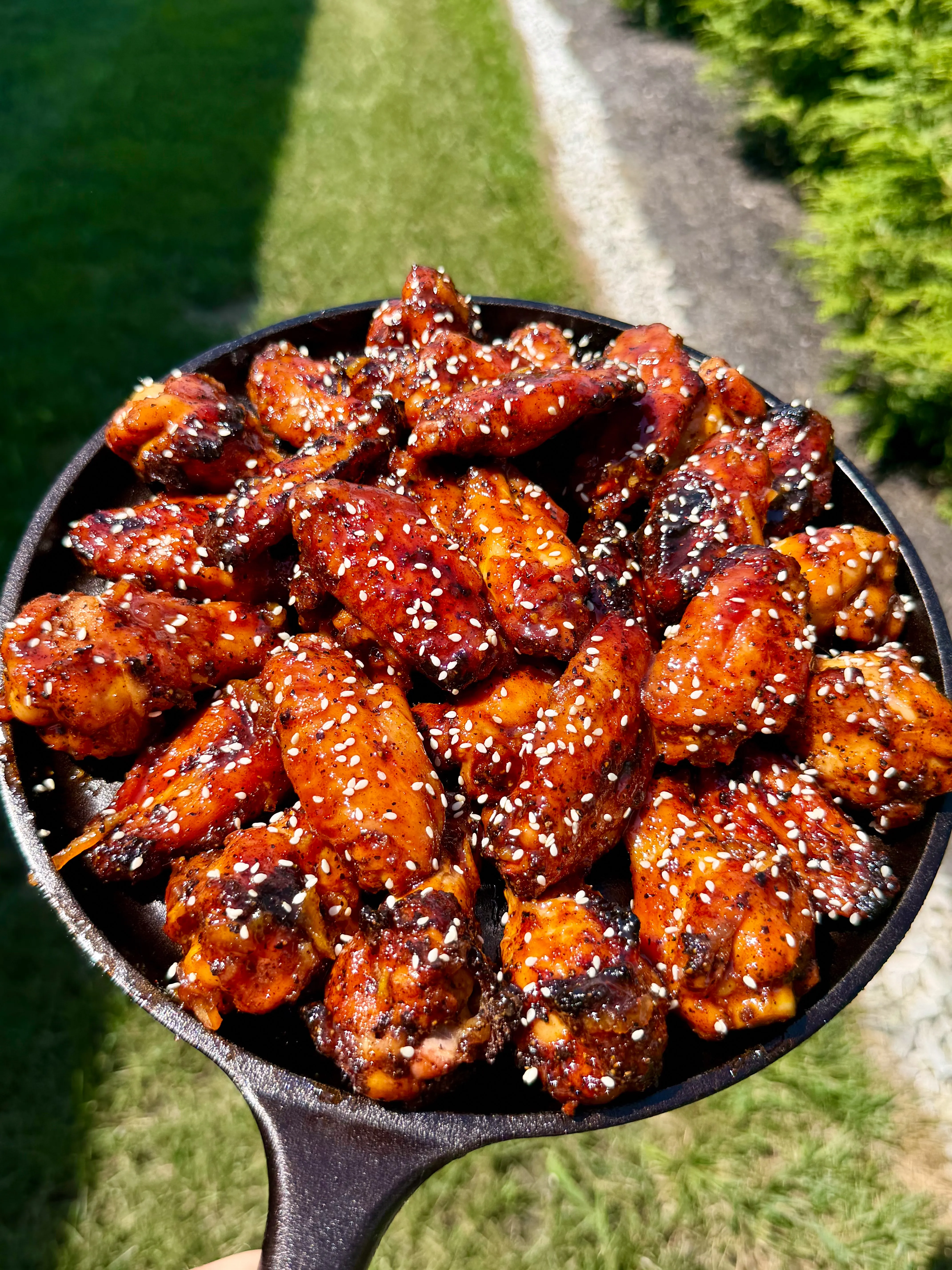 Orange gochujang smoked chicken wings glazed with sesame seeds in a cast iron skillet