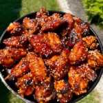 Glazed orange gochujang BBQ smoked chicken wings topped with sesame seeds in a cast iron skillet
