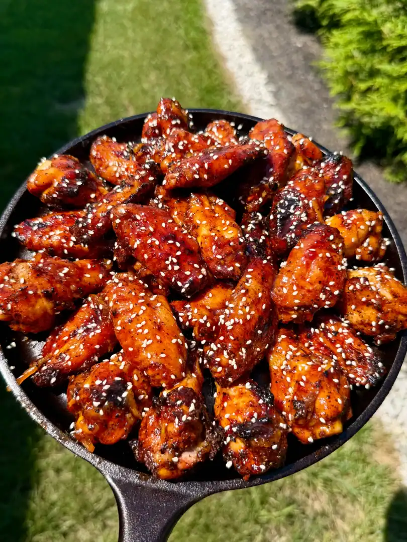Glazed orange gochujang BBQ smoked chicken wings topped with sesame seeds in a cast iron skillet