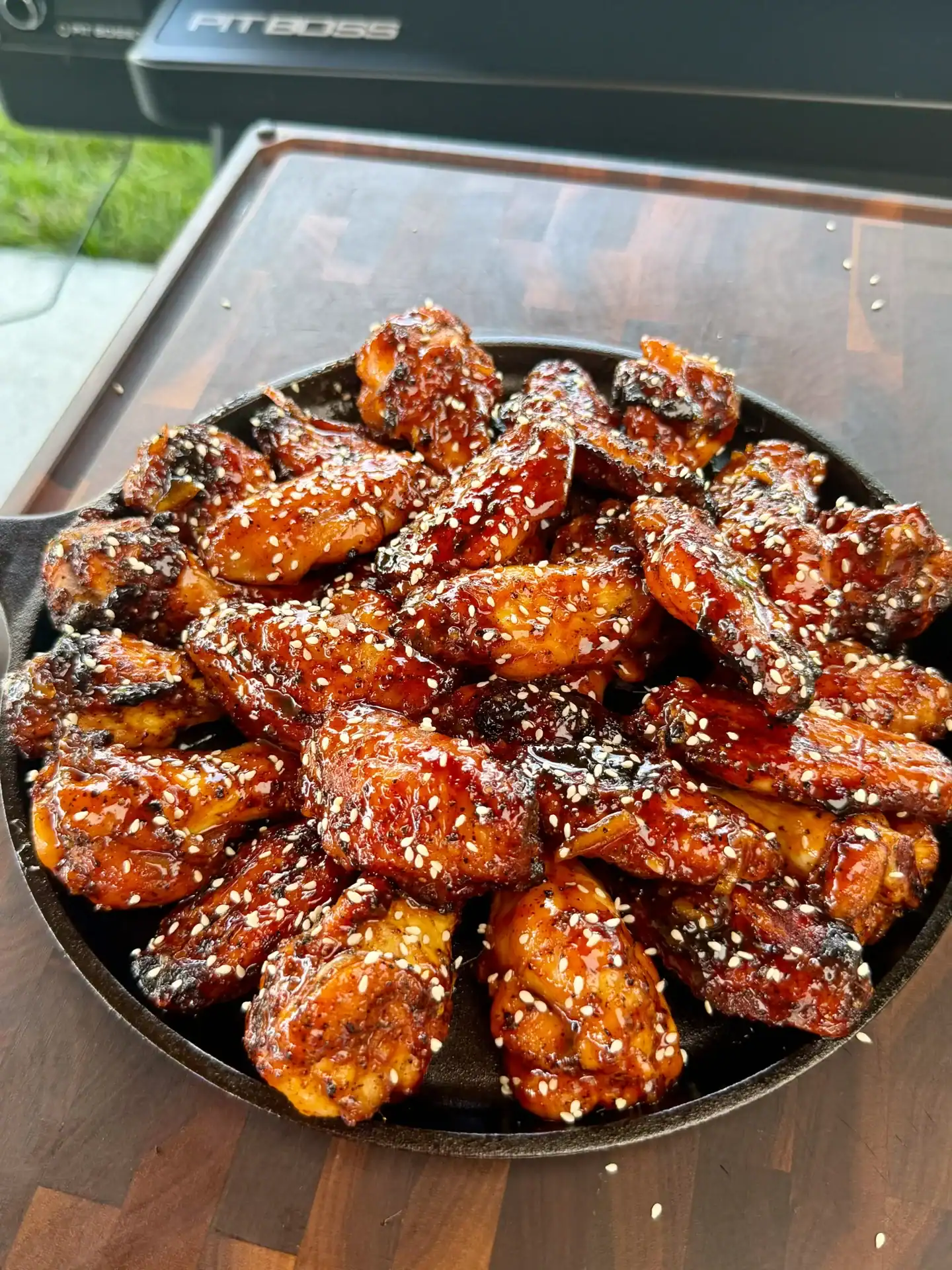 Glossy orange gochujang BBQ smoked chicken wings topped with sesame seeds in a cast iron skillet.