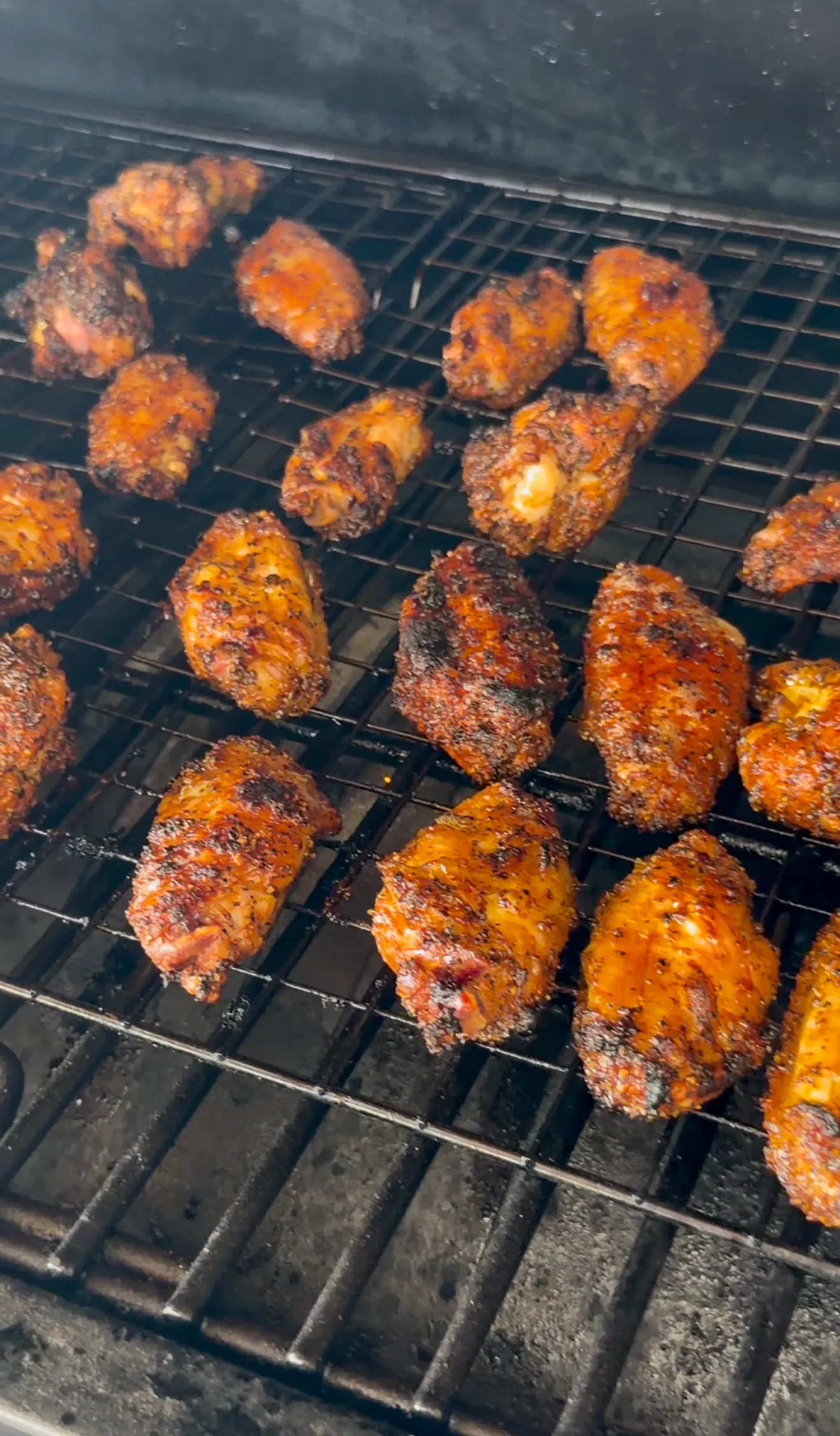 Wings with a caramelized spice crust cooking on dark smoker grates