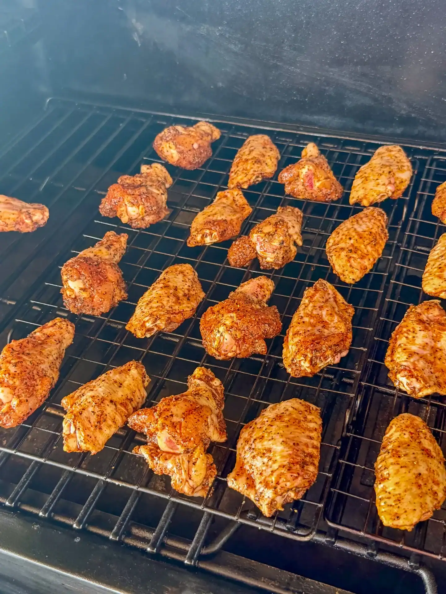 Seasoned orange gochujang BBQ chicken wings arranged on smoker grates with visible spice rub and smoke.