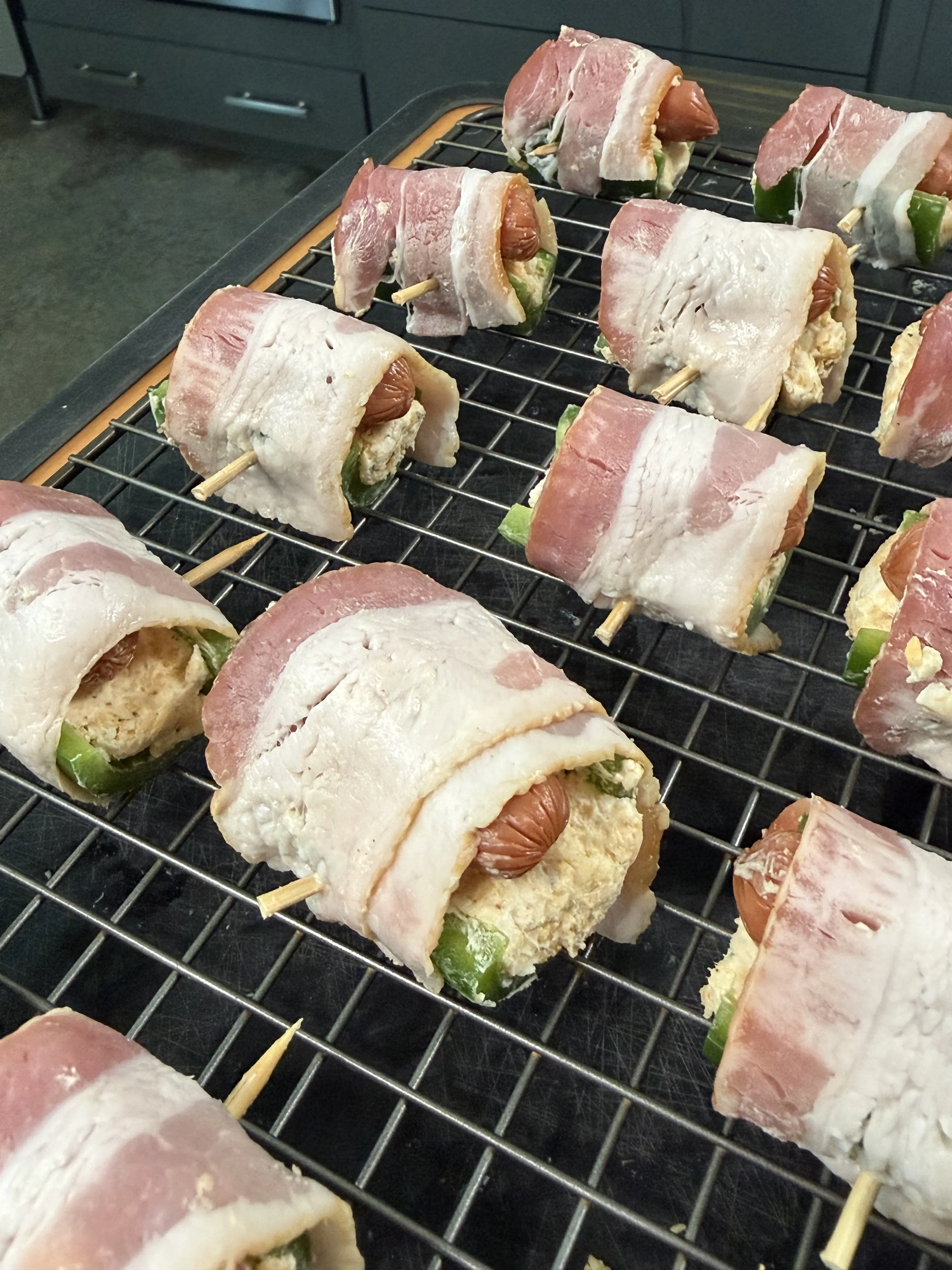 Raw bacon wrapped jalapeño smokie bombs secured with toothpicks on a wire rack