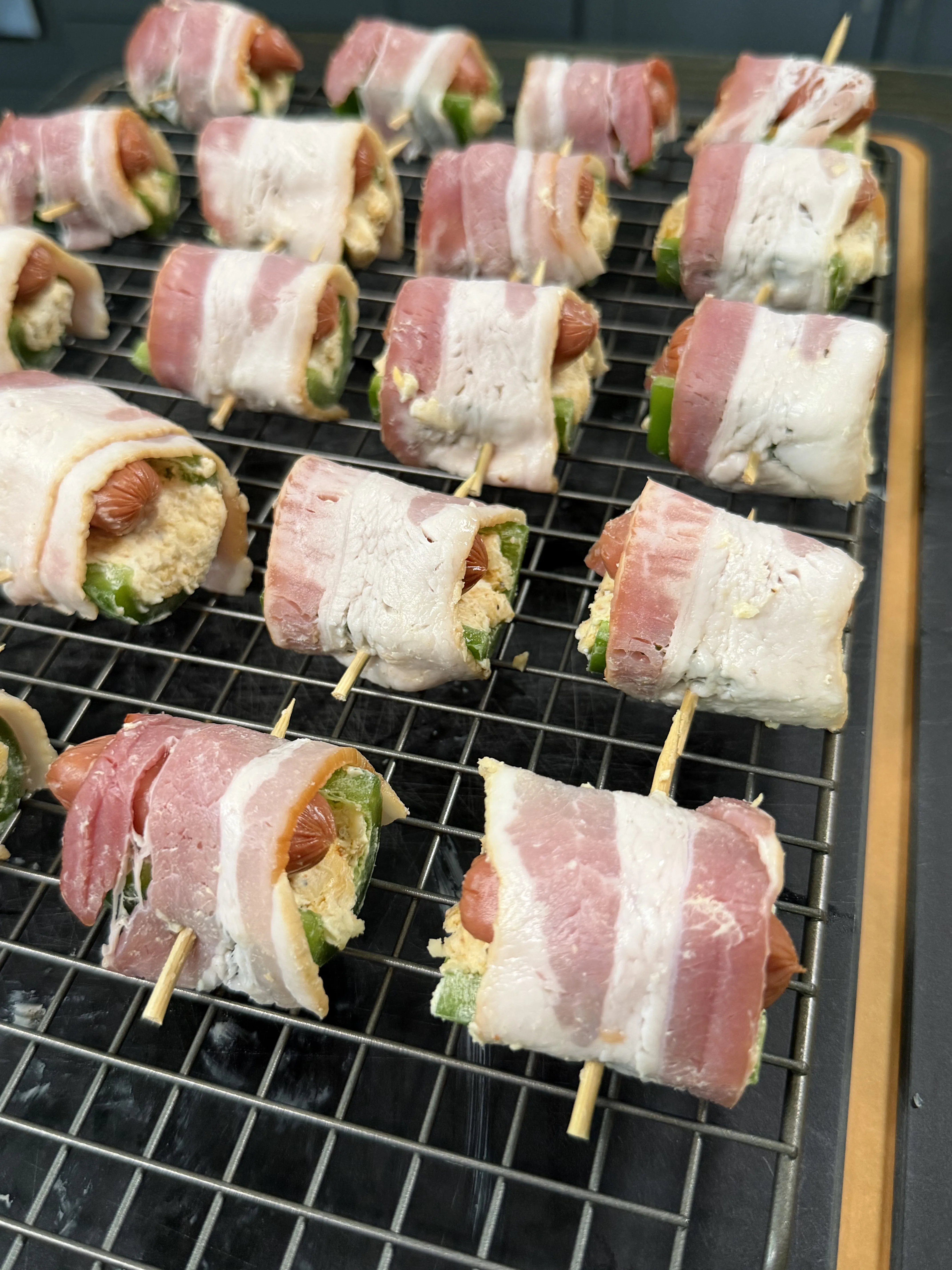 Raw bacon wrapped jalapeño smokie bombs secured with toothpicks on a wire rack ready to smoke