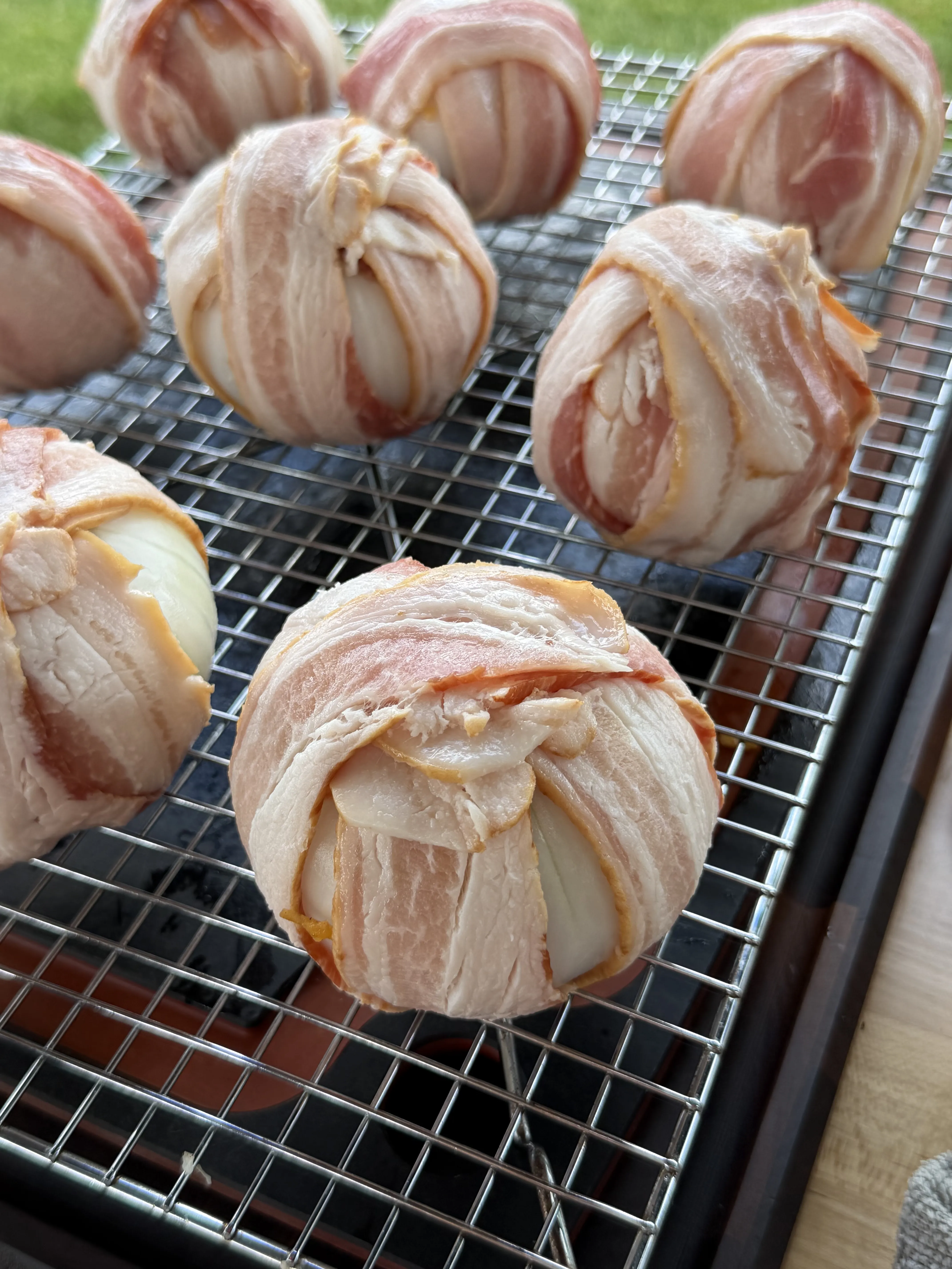 Bacon wrapped onion bombs arranged on a wire rack ready for the smoker