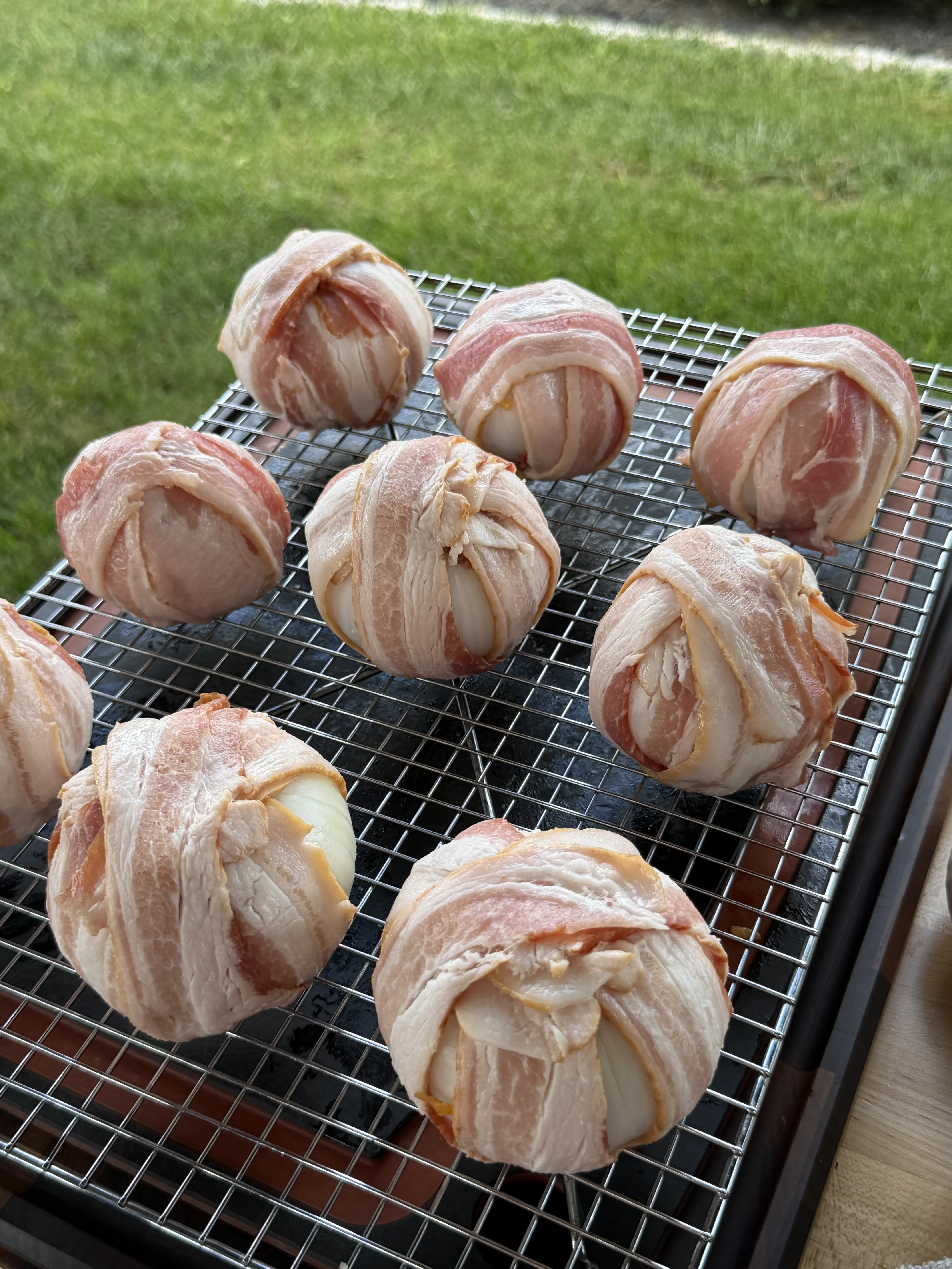 Nine bacon wrapped onion bombs lined up on a wire smoker rack before the cook