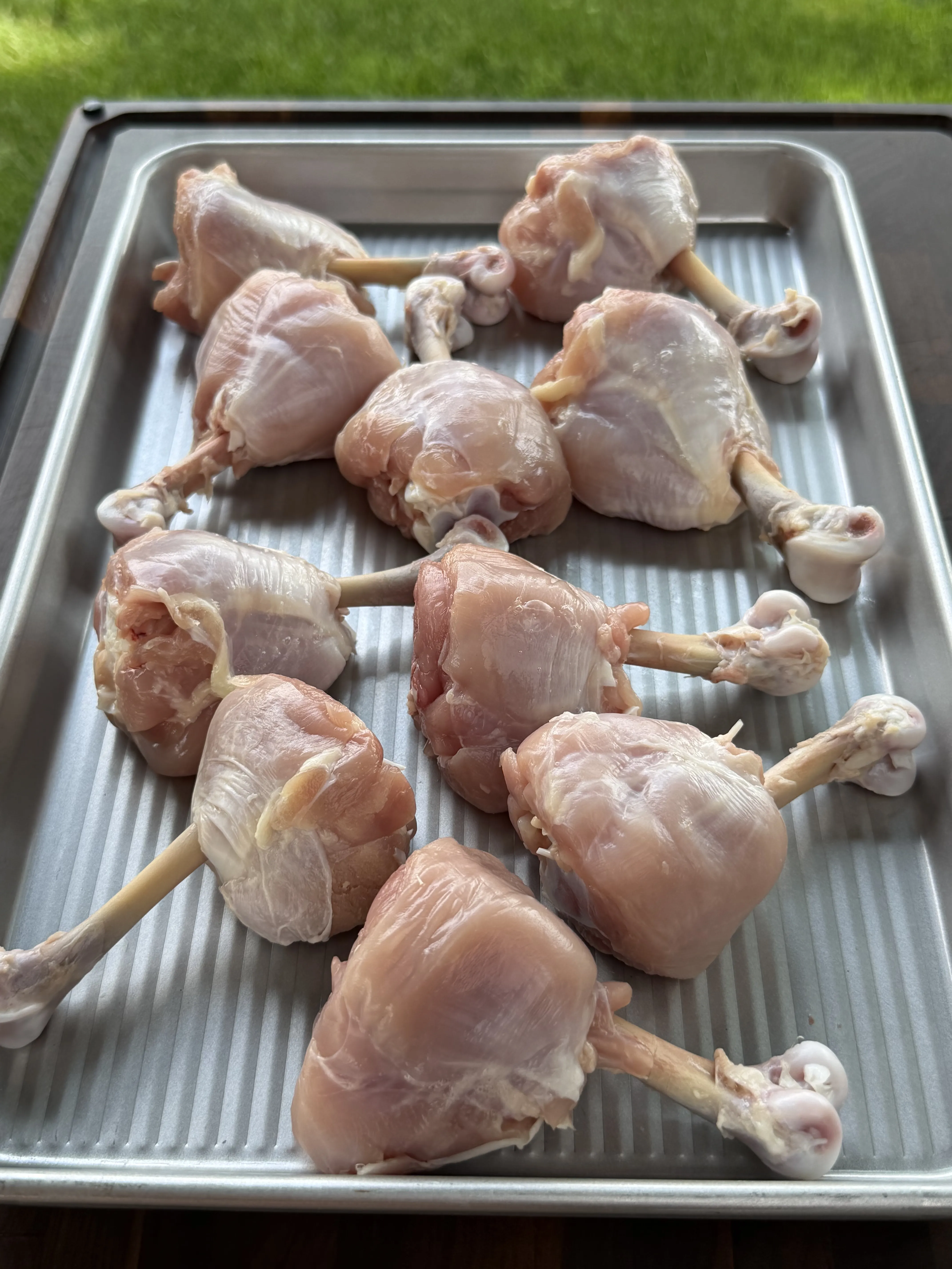 Raw frenched chicken drumstick lollipops on a baking sheet, ready to be wrapped in bacon