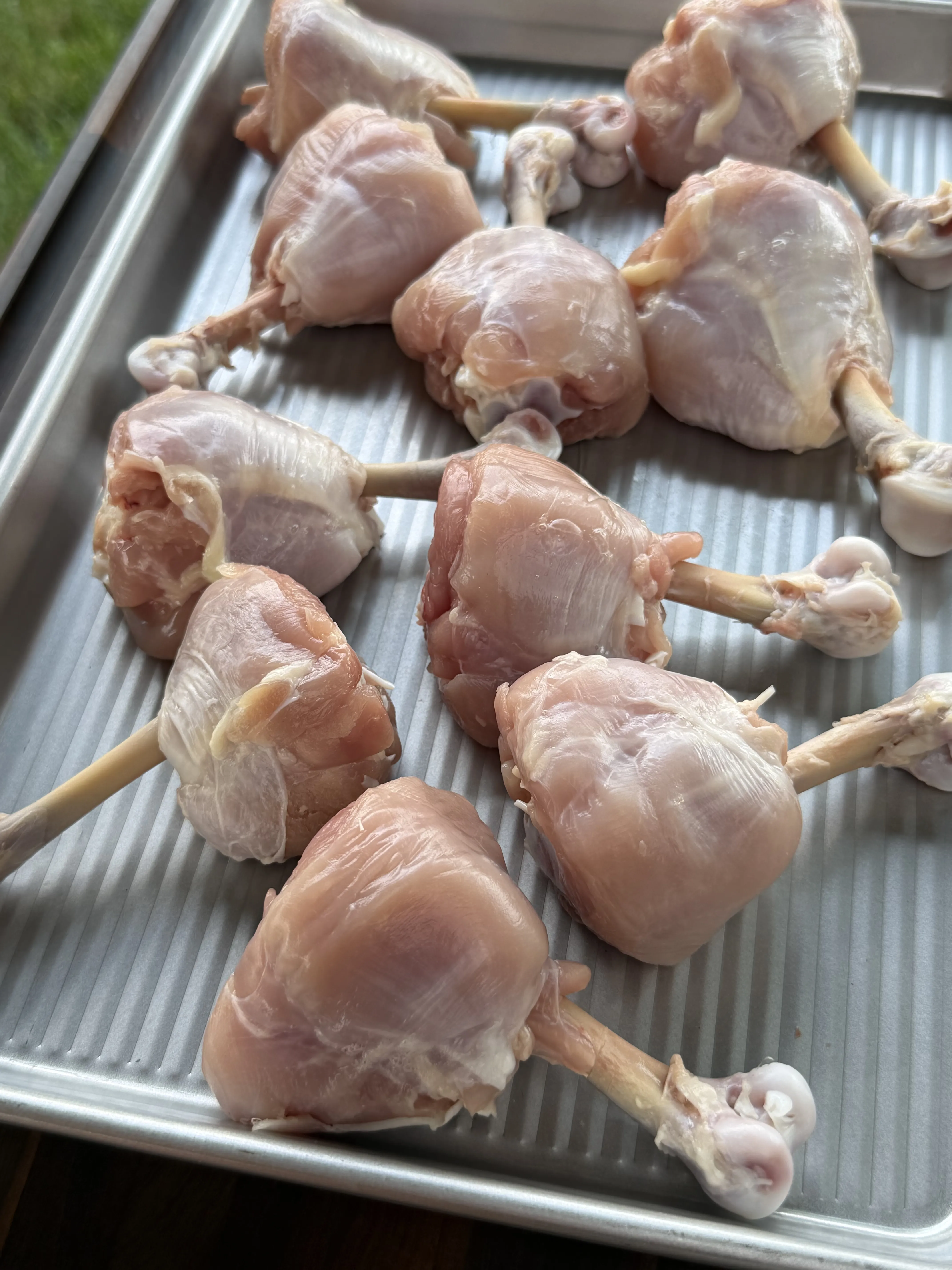 Raw chicken lollipops with frenched bones on a baking sheet, ready to wrap in bacon