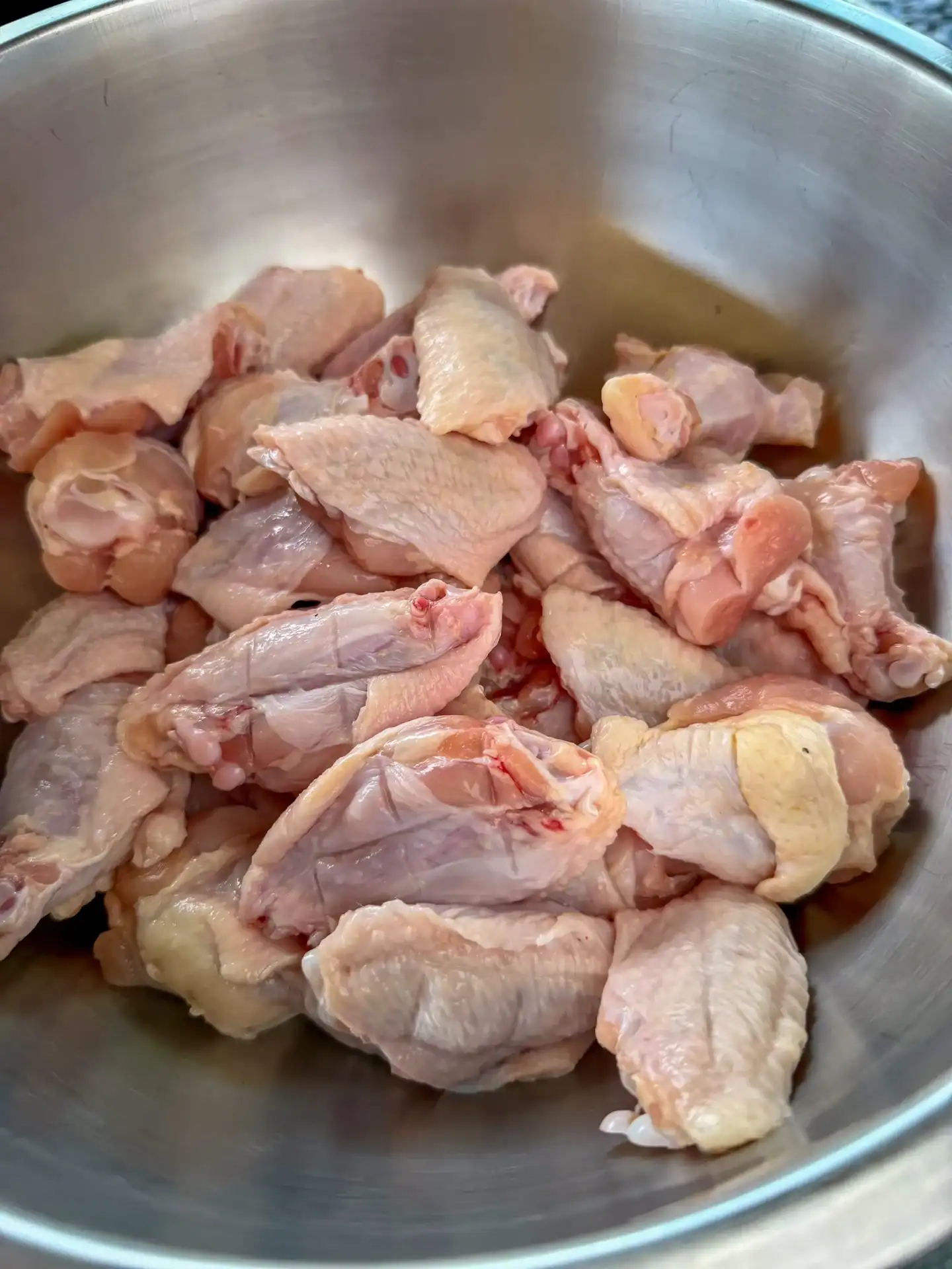 Raw chicken wings piled in a large stainless steel mixing bowl, ready to be seasoned for smoked wings.