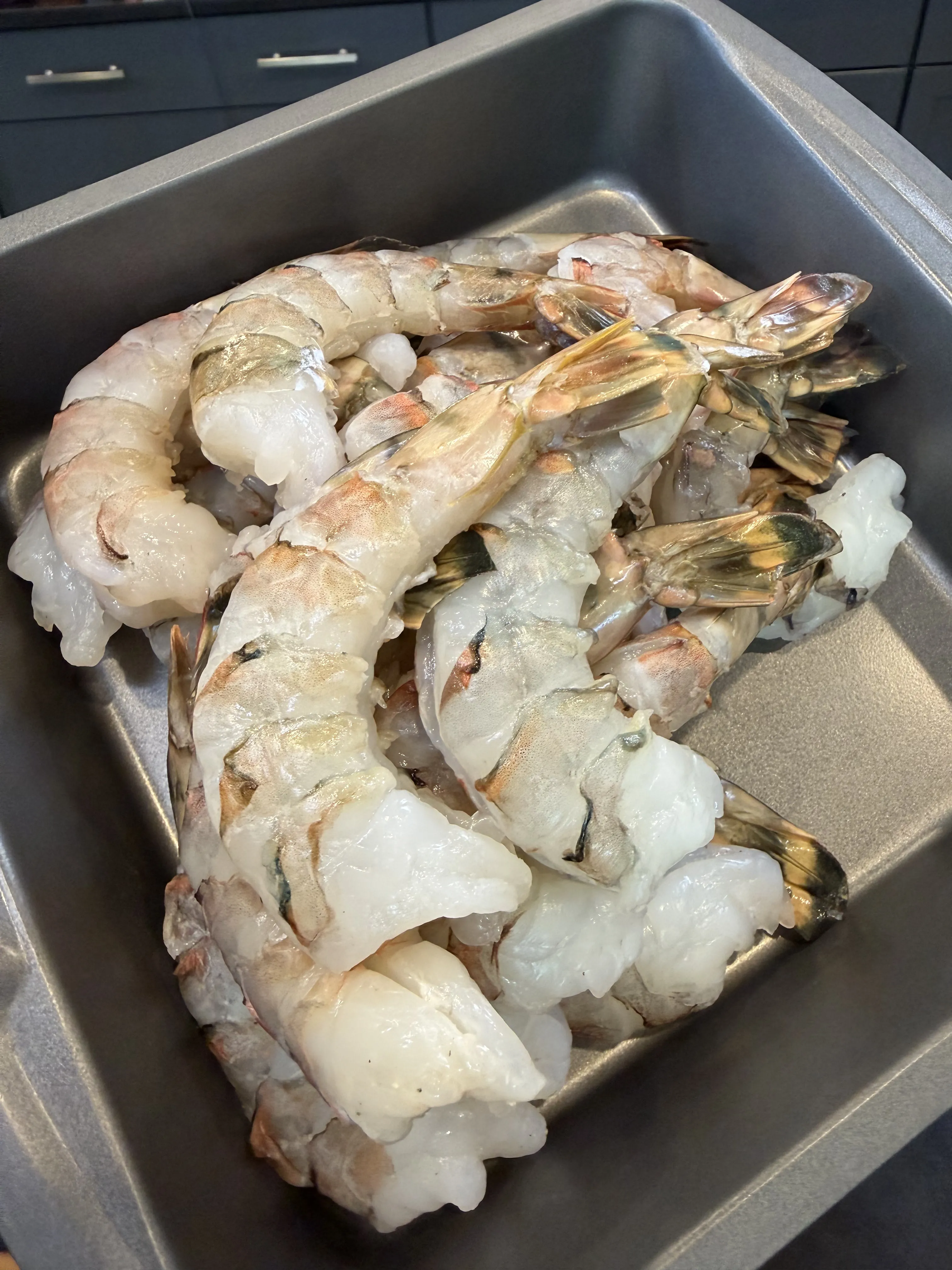 Raw tail-on jumbo shrimp in a metal pan, ready to be skewered and smoked