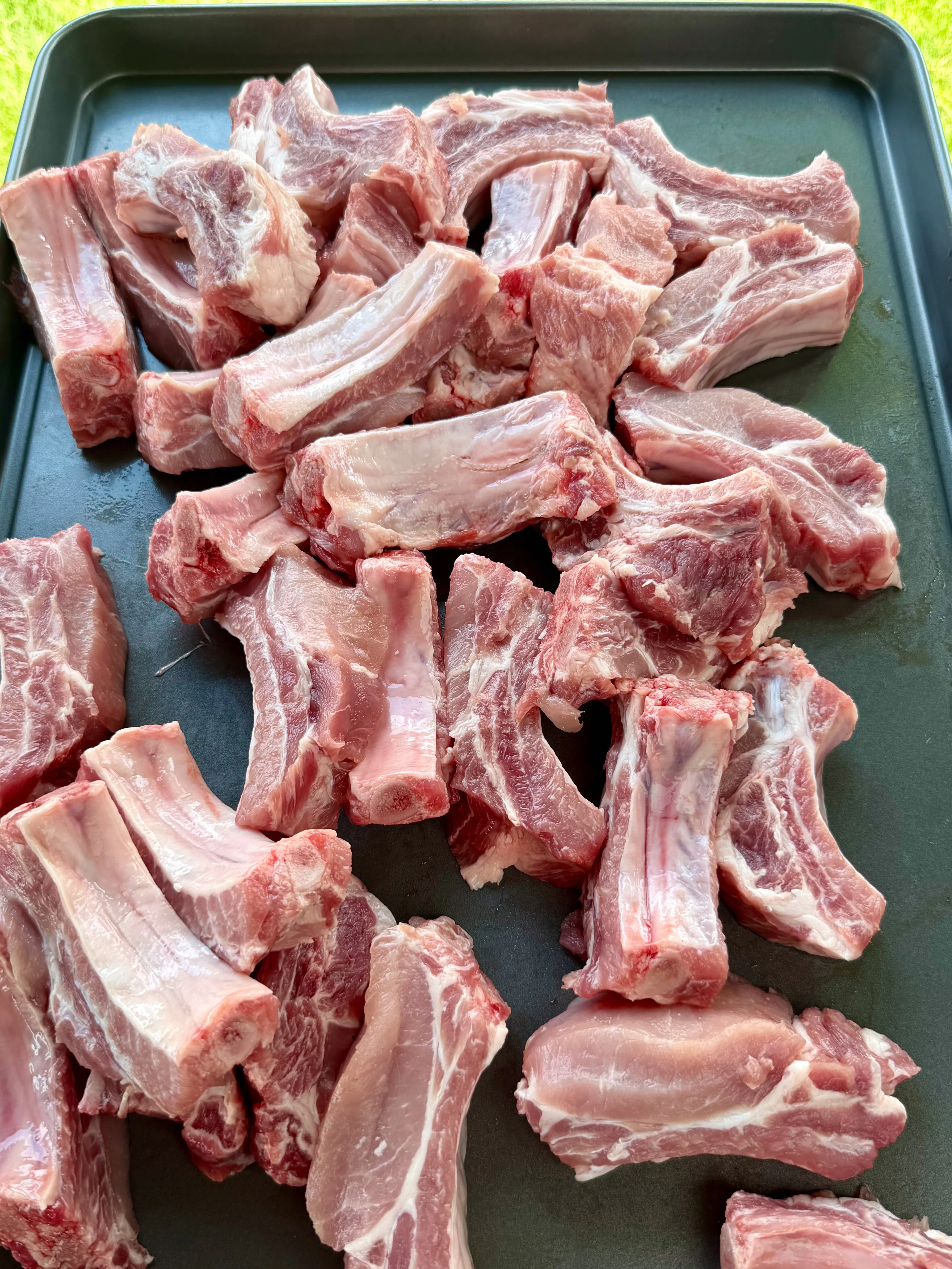 Raw pork ribs cut into individual party ribs on a dark baking sheet, ready for smoking