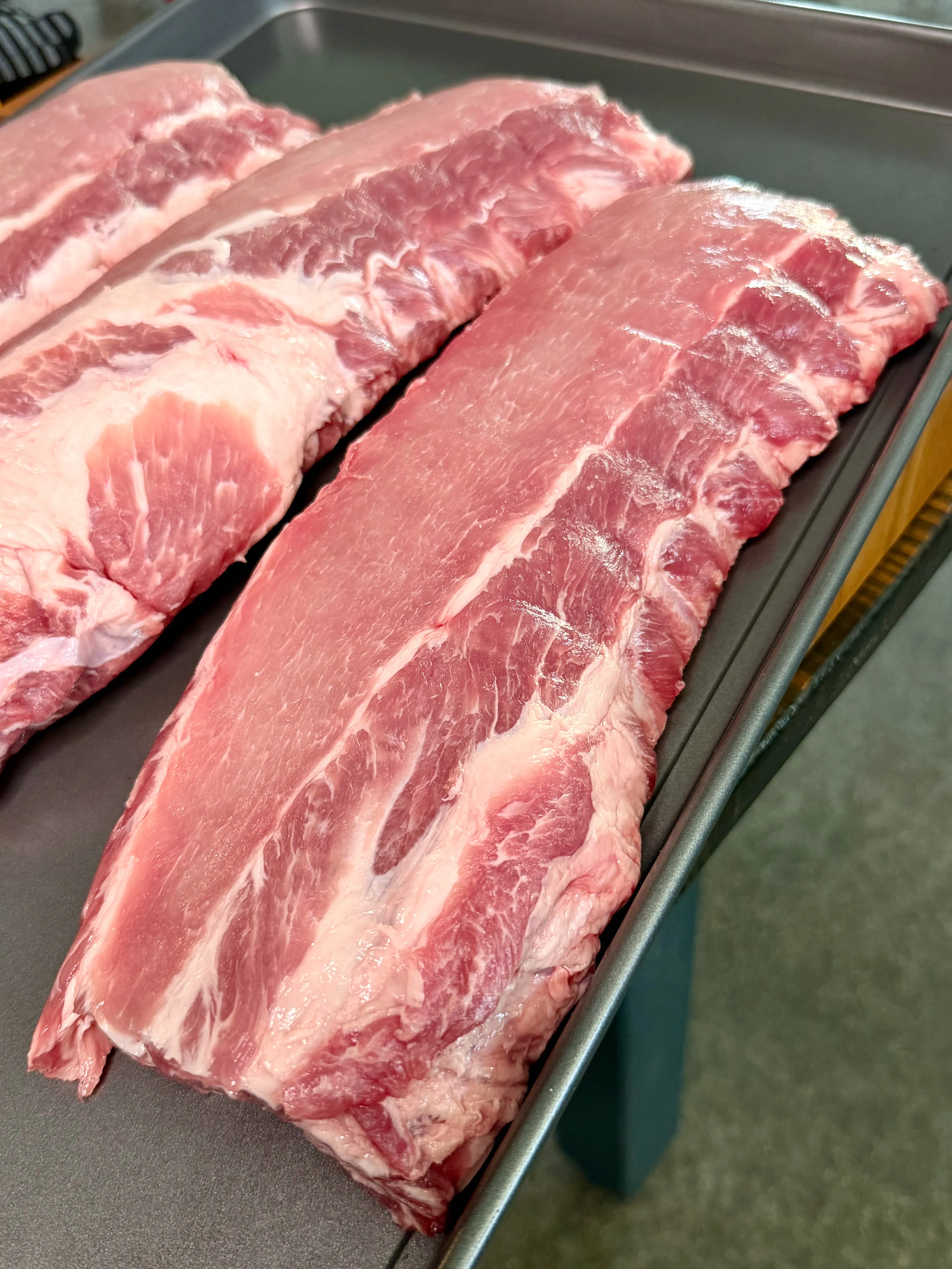Two raw pork spare rib racks on a metal baking sheet, ready to be seasoned for smoked party ribs