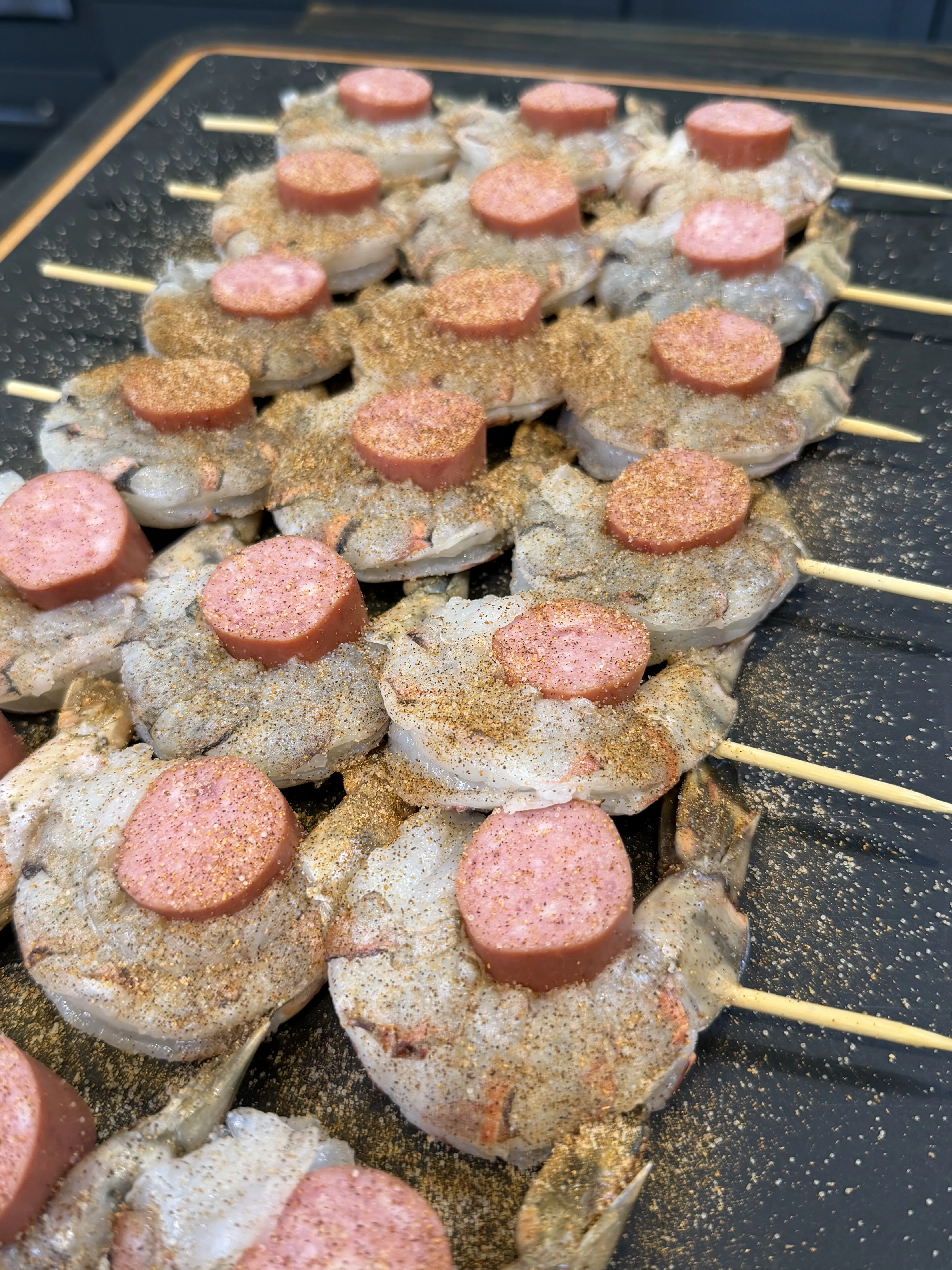 Raw smoked shrimp and sausage skewers seasoned with Creole rub on a dark grilling tray, ready to smoke