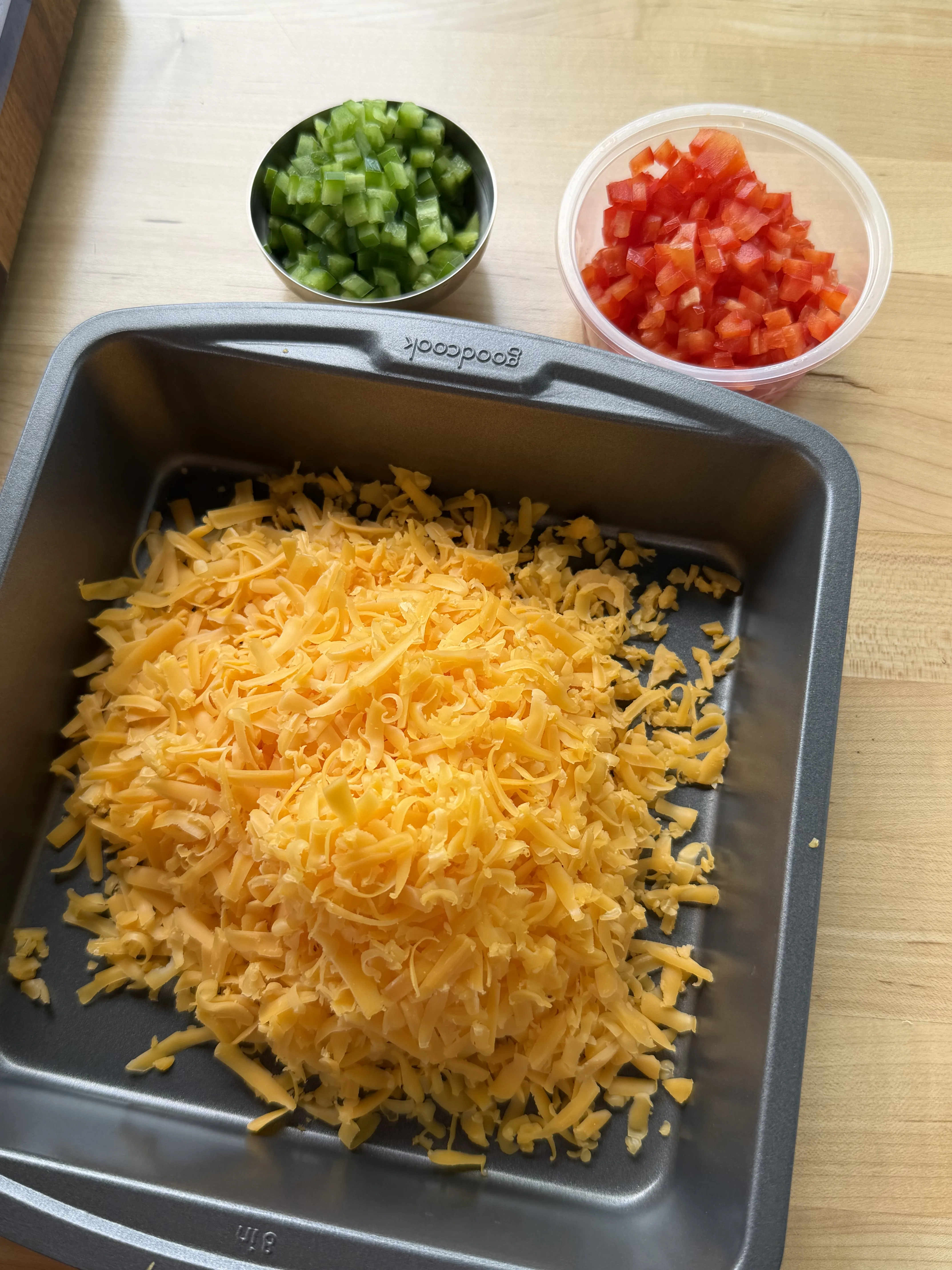 Shredded cheddar and diced peppers prepped in a baking pan for the filling
