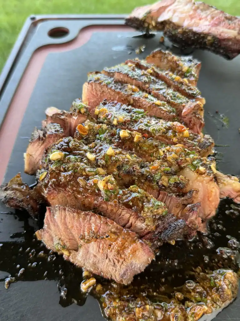 Sliced grilled steak topped with melted chili parmesan compound butter on a dark cutting board