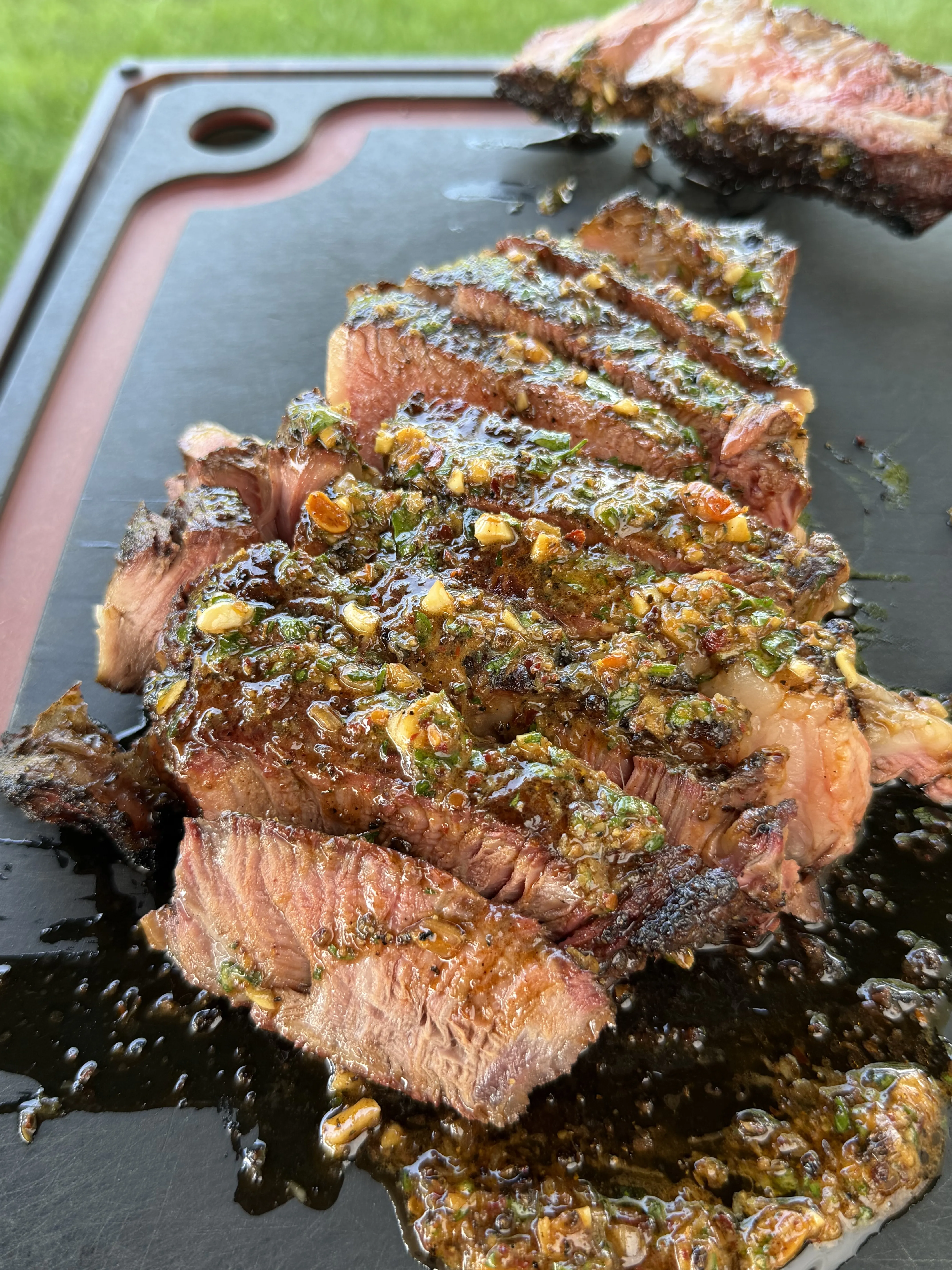 Sliced grilled steak topped with melted chili parmesan compound butter on a dark board