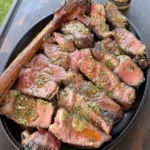 Sliced grilled steak topped with melting herb compound butter in a cast iron dish with Weber seasoning