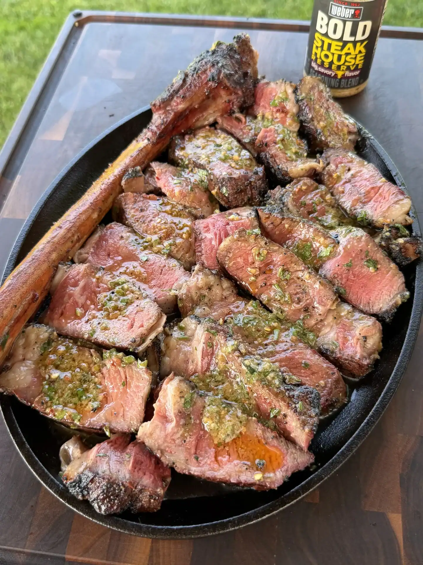 Sliced grilled steak topped with melting herb compound butter in a cast iron dish with Weber seasoning