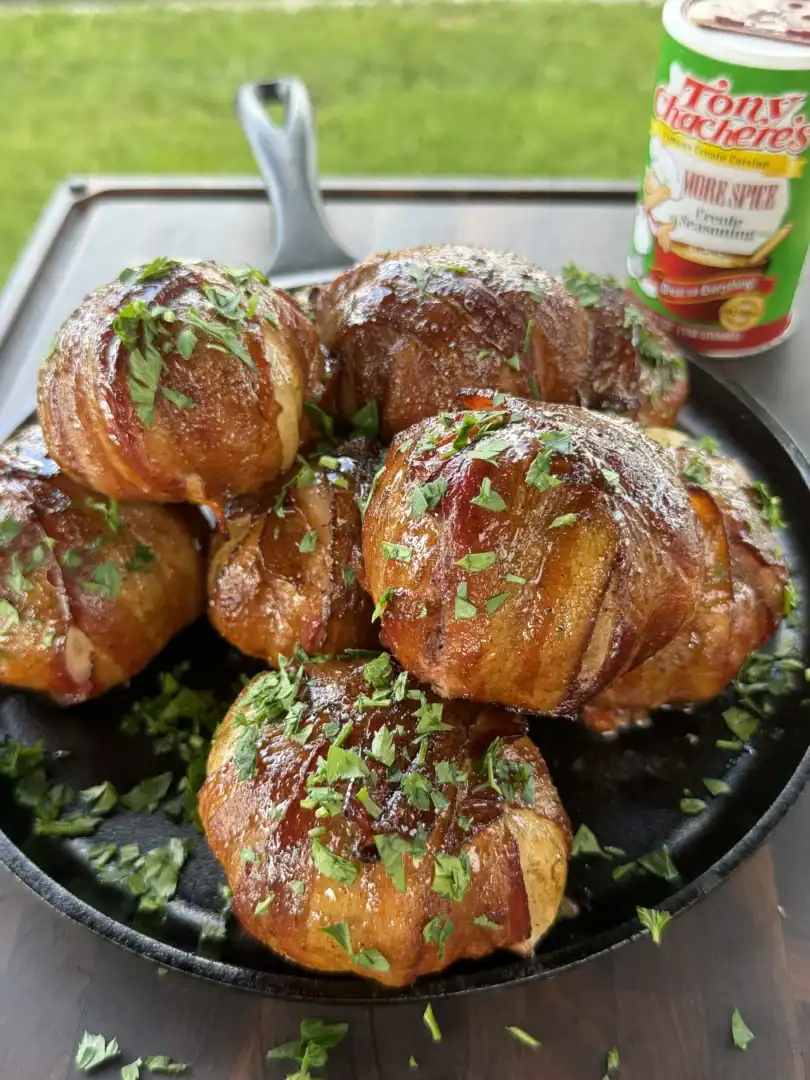 Smoked bacon cheeseburger onion bombs in a cast iron skillet, garnished with fresh parsley, with Tony Chachere's seasoning nearby