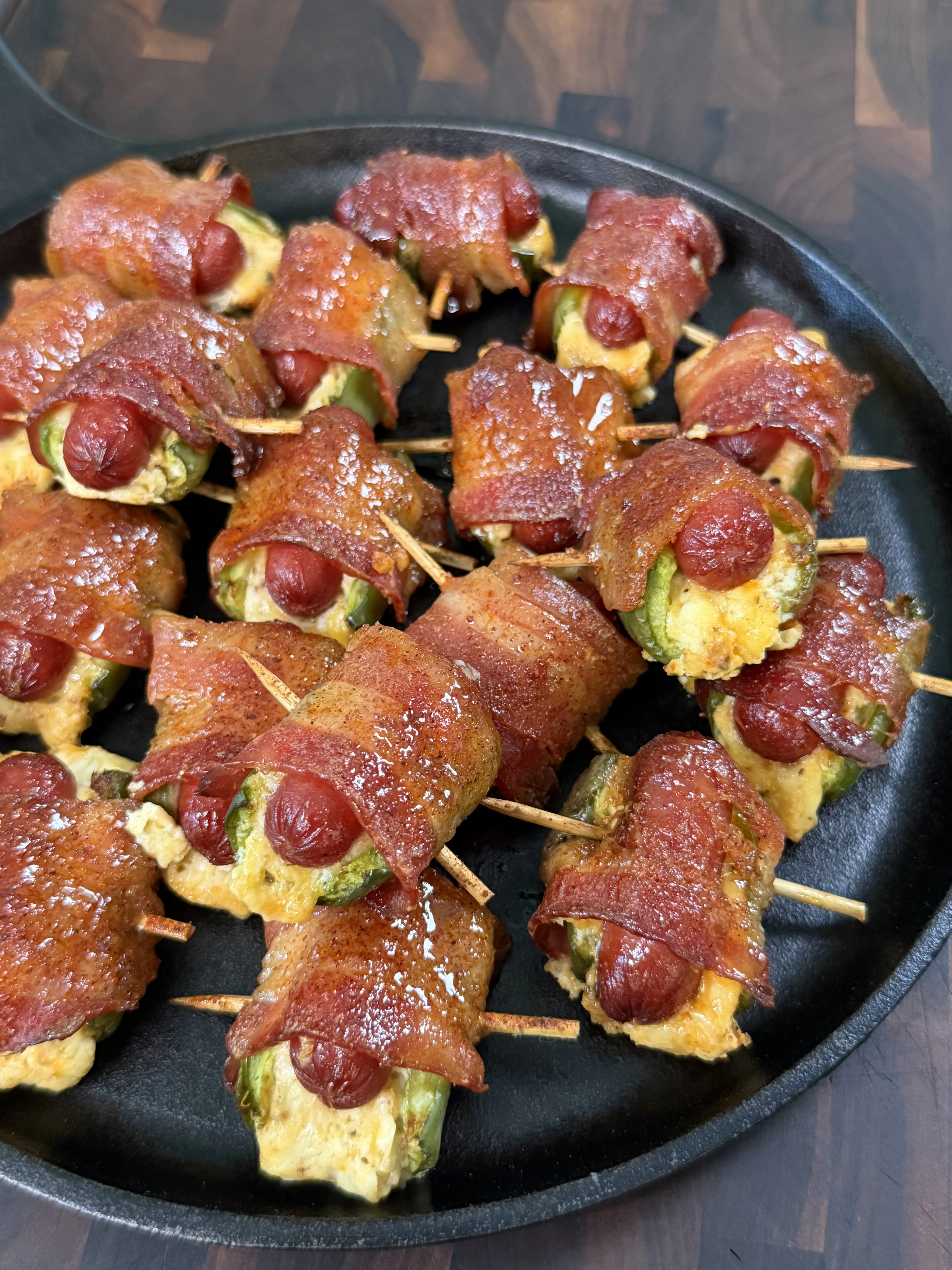 Bacon wrapped jalapeño smokie bombs with cream cheese filling on a cast iron platter