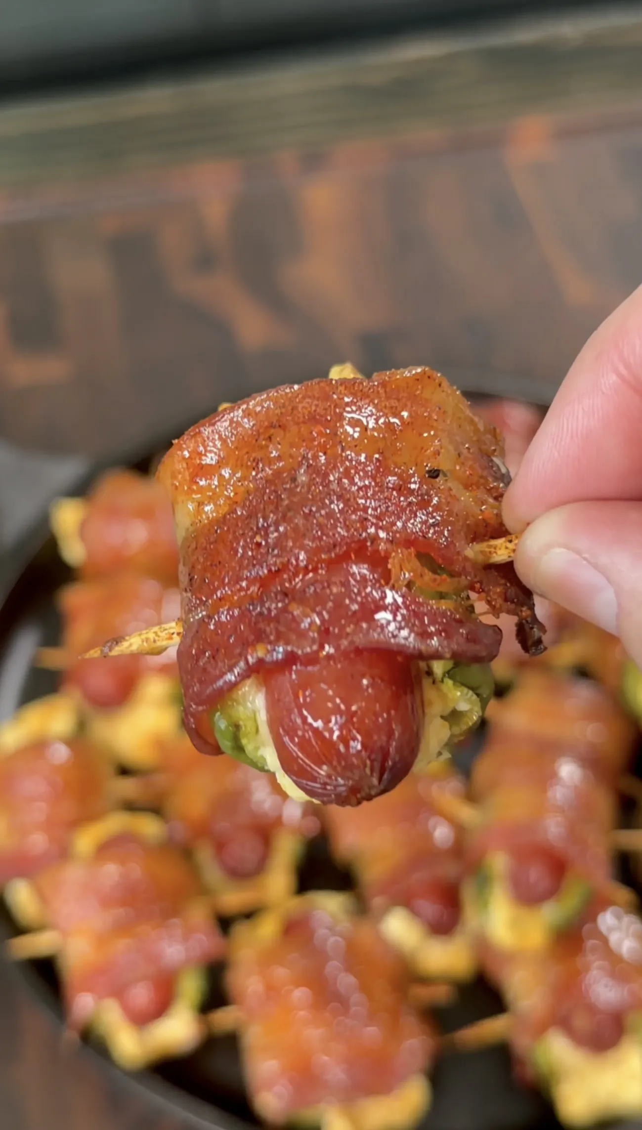 Smoked bacon wrapped jalapeño smokie bomb with glazed crispy bacon held over a pan of more