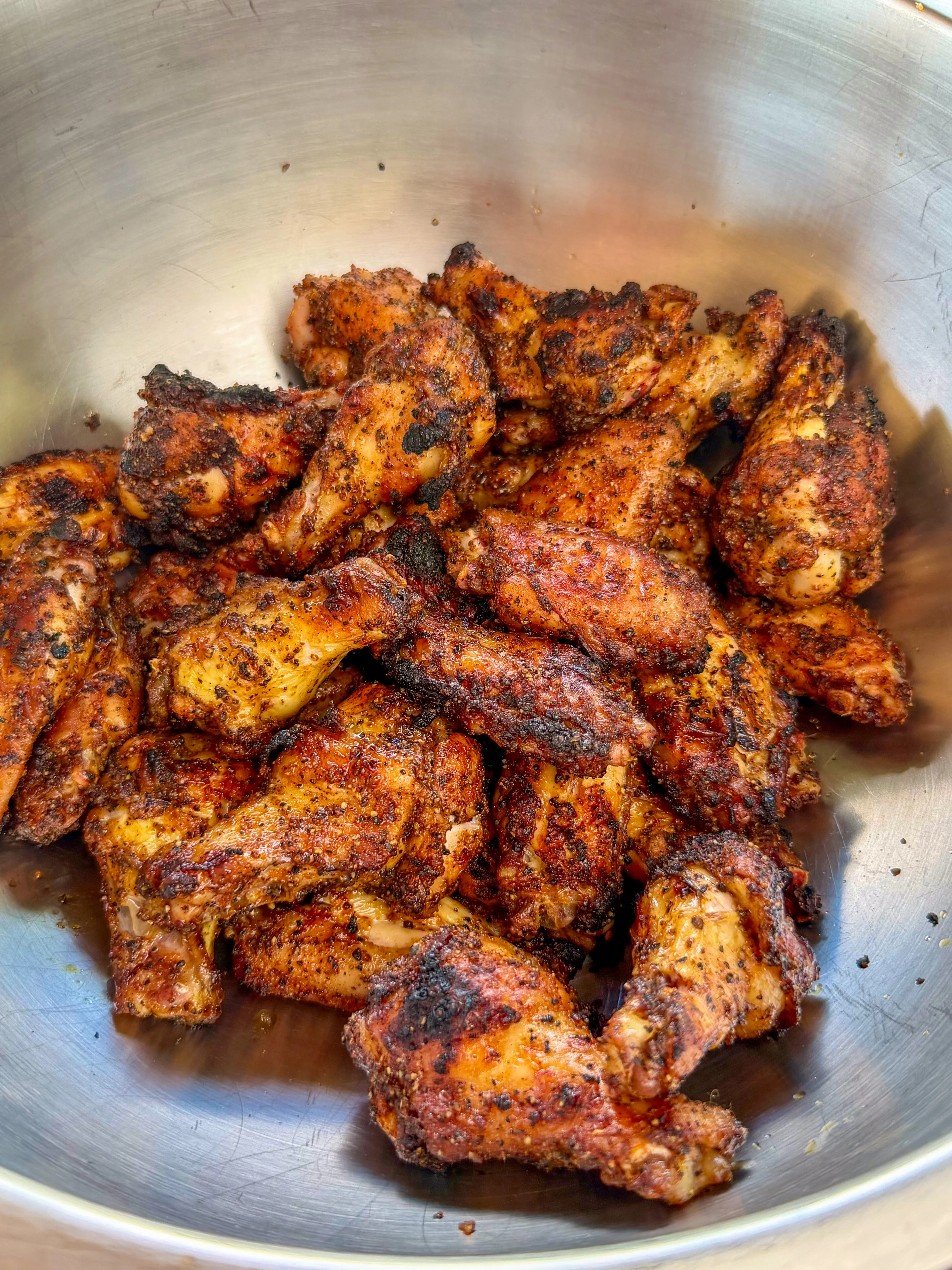 Dry-rubbed chicken wings piled in a stainless steel bowl after seasoning