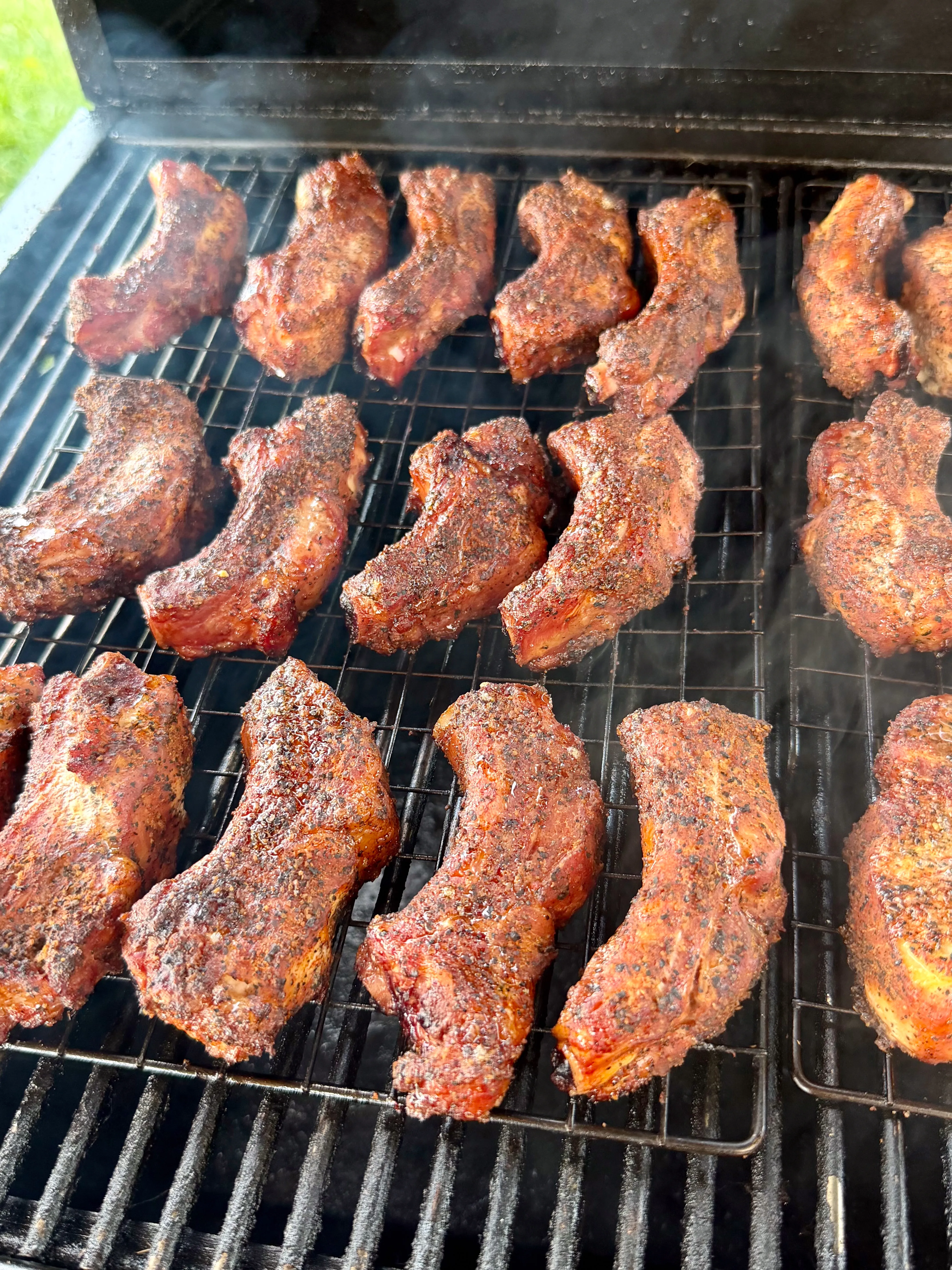 Dry-rubbed smoked party ribs arranged on smoker grates with visible smoke