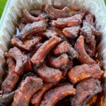Smoky dill pickle hot honey party ribs piled high in a disposable aluminum foil pan with rich juices