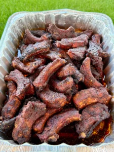 Smoky dill pickle hot honey party ribs piled high in a disposable aluminum foil pan with rich juices