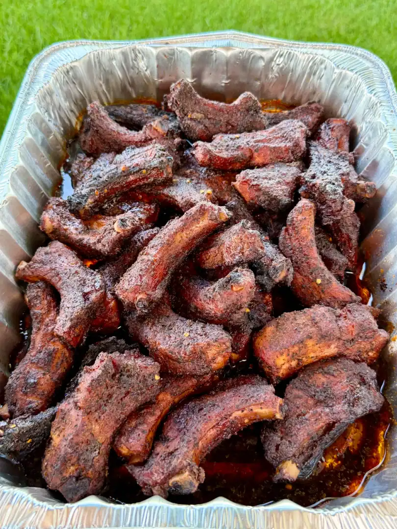 Smoky dill pickle hot honey party ribs piled high in a disposable aluminum foil pan with rich juices