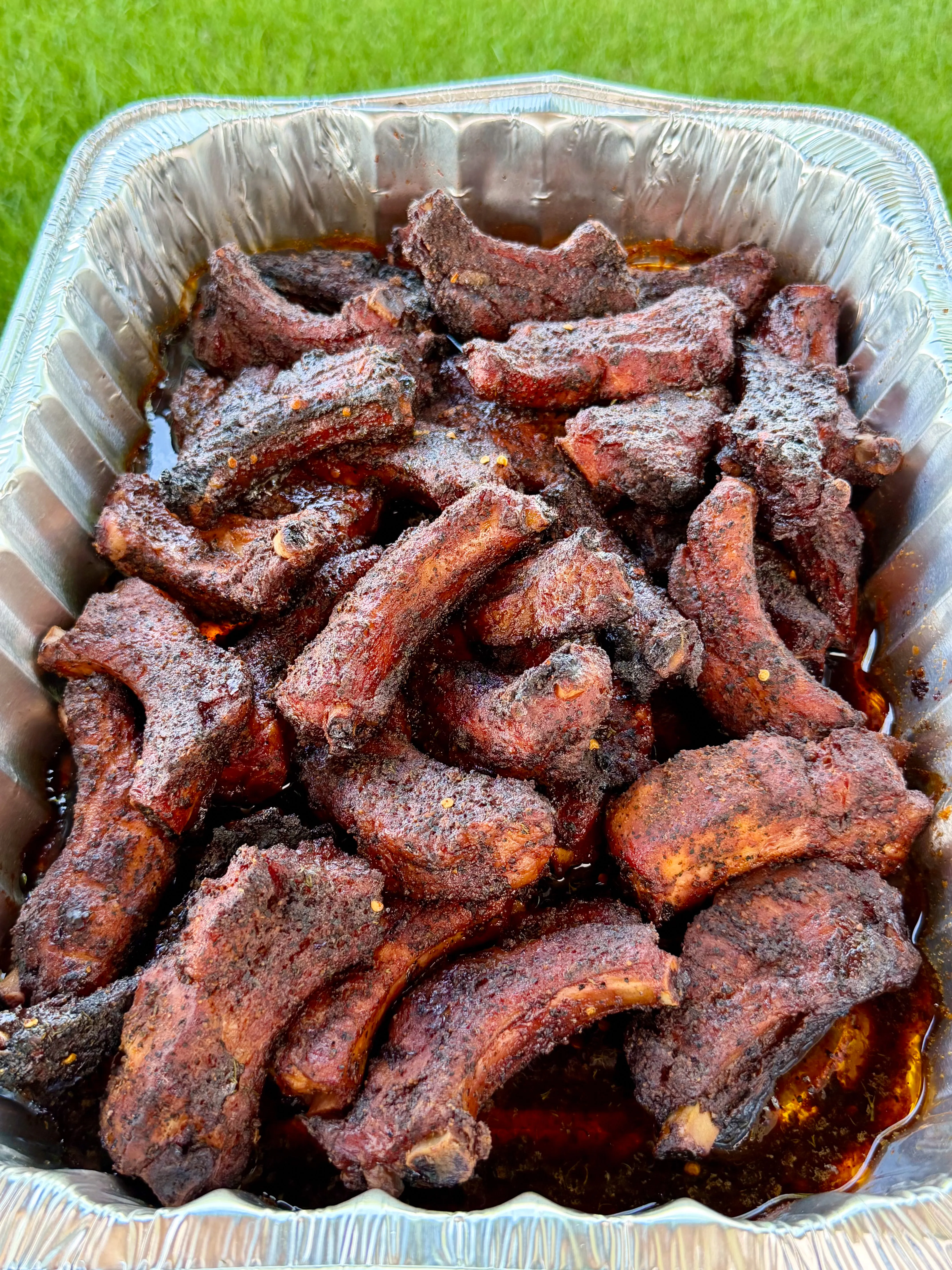 Smoky party ribs piled high in a disposable aluminum foil pan with rich juices